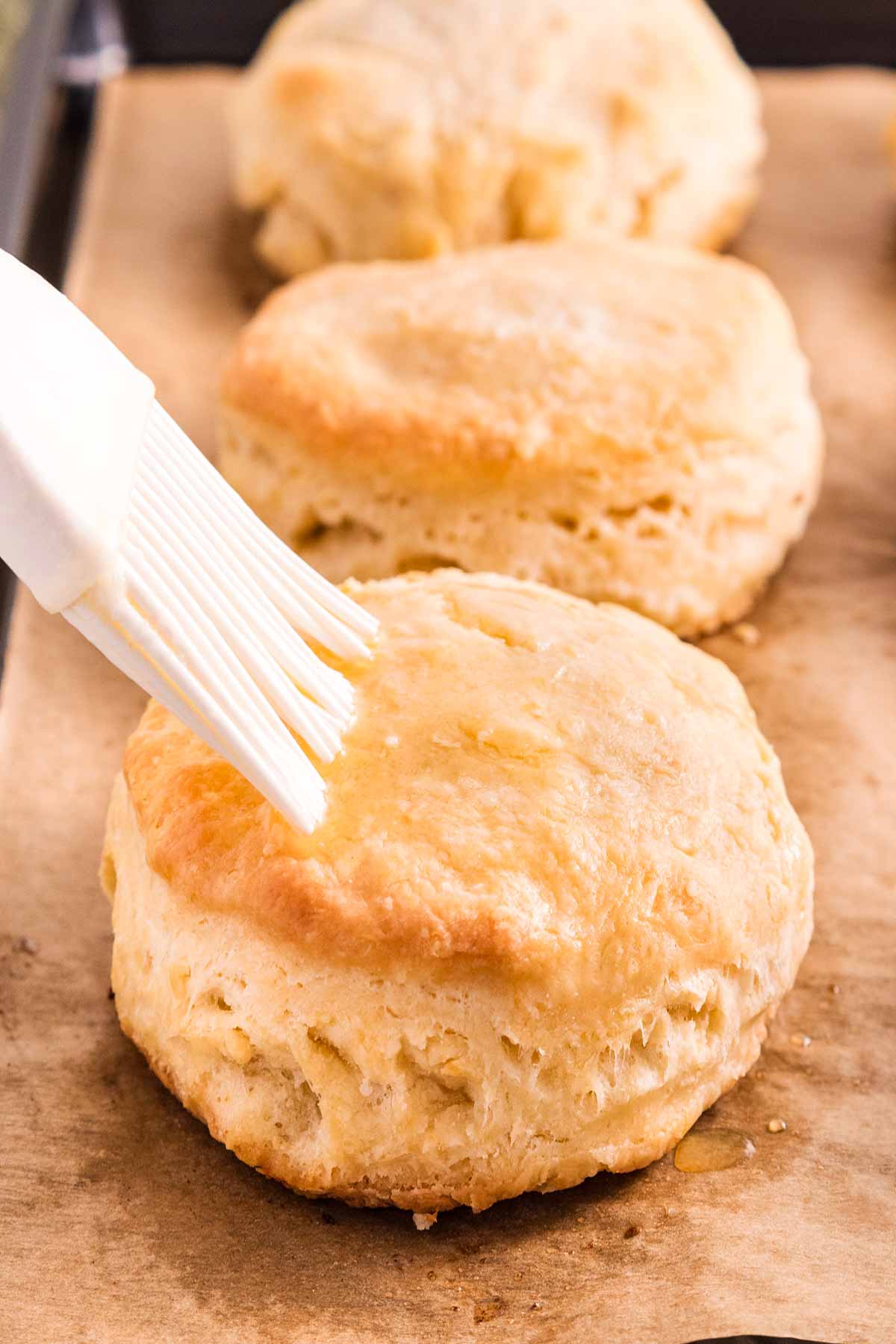 frontal view of silicone brush brushing butter over baked biscuit