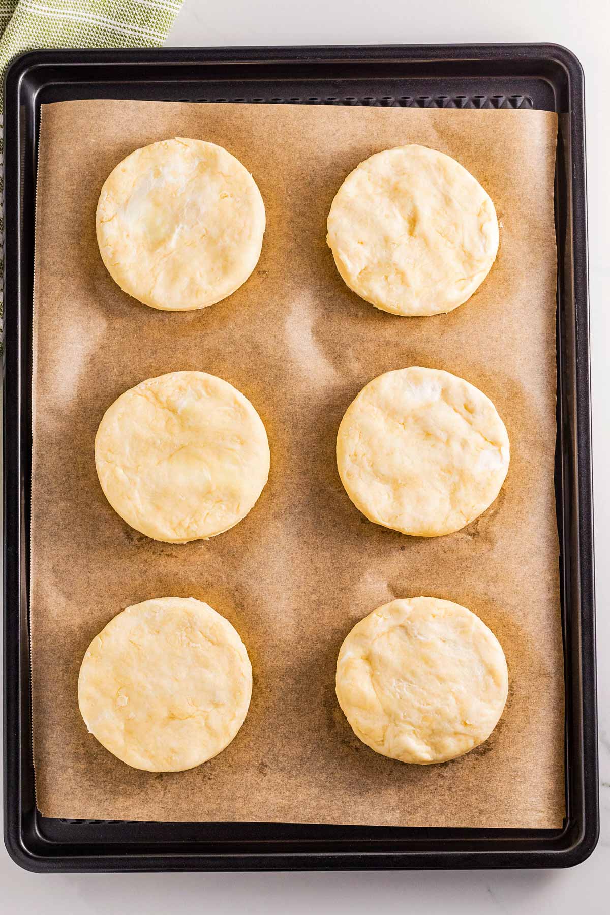 overhead view of six unbaked biscuits on top of parchment lined baking pan