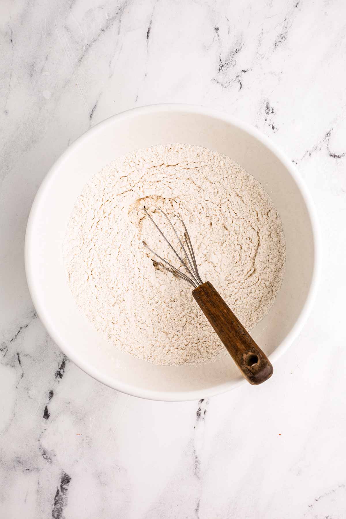 overhead view of flour in white bowl with whisk