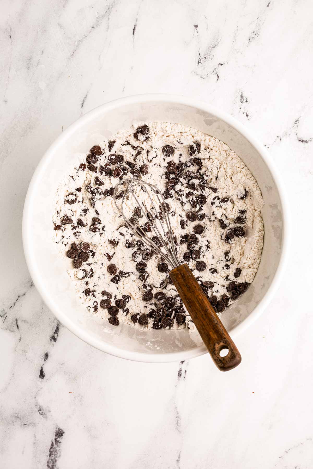 overhead view of flour  and chocolate chips in white bowl with whisk