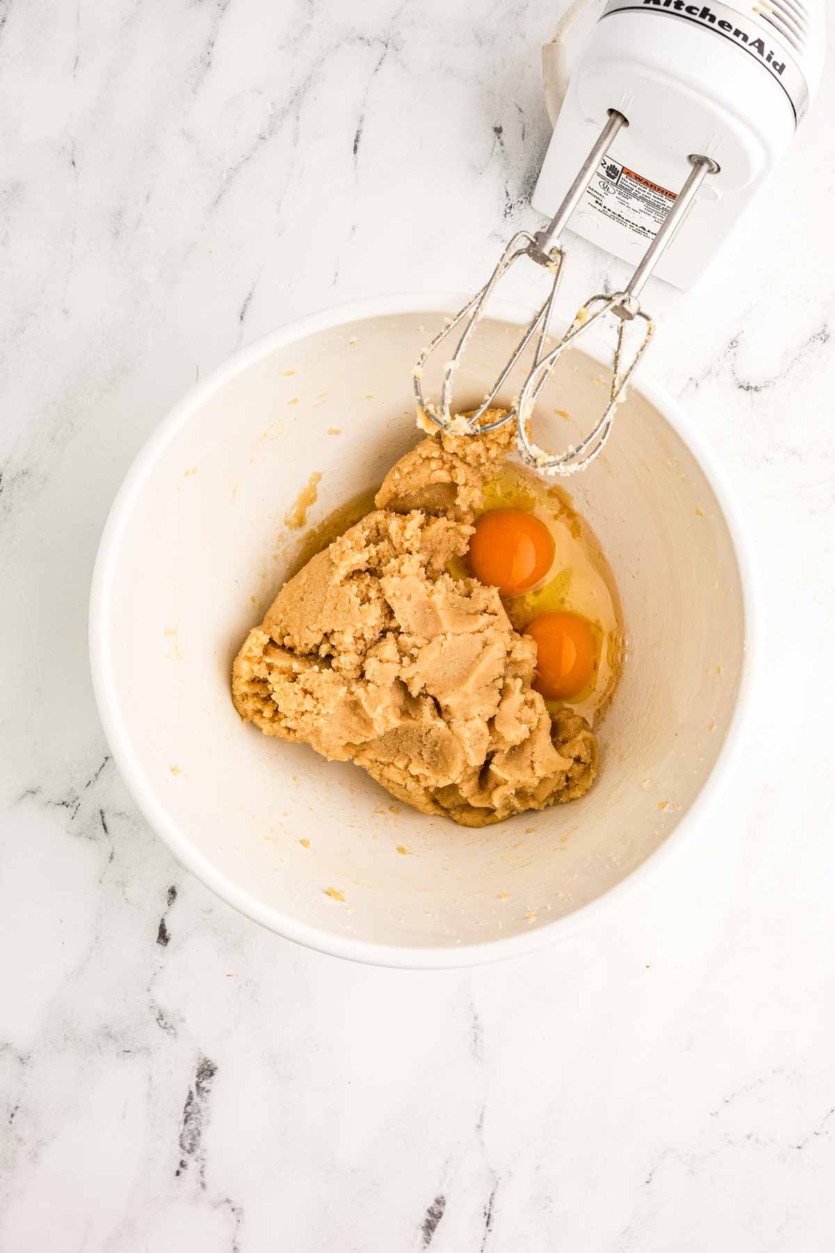 overhead view of eggs and dough in bowl with electric mixer next to it