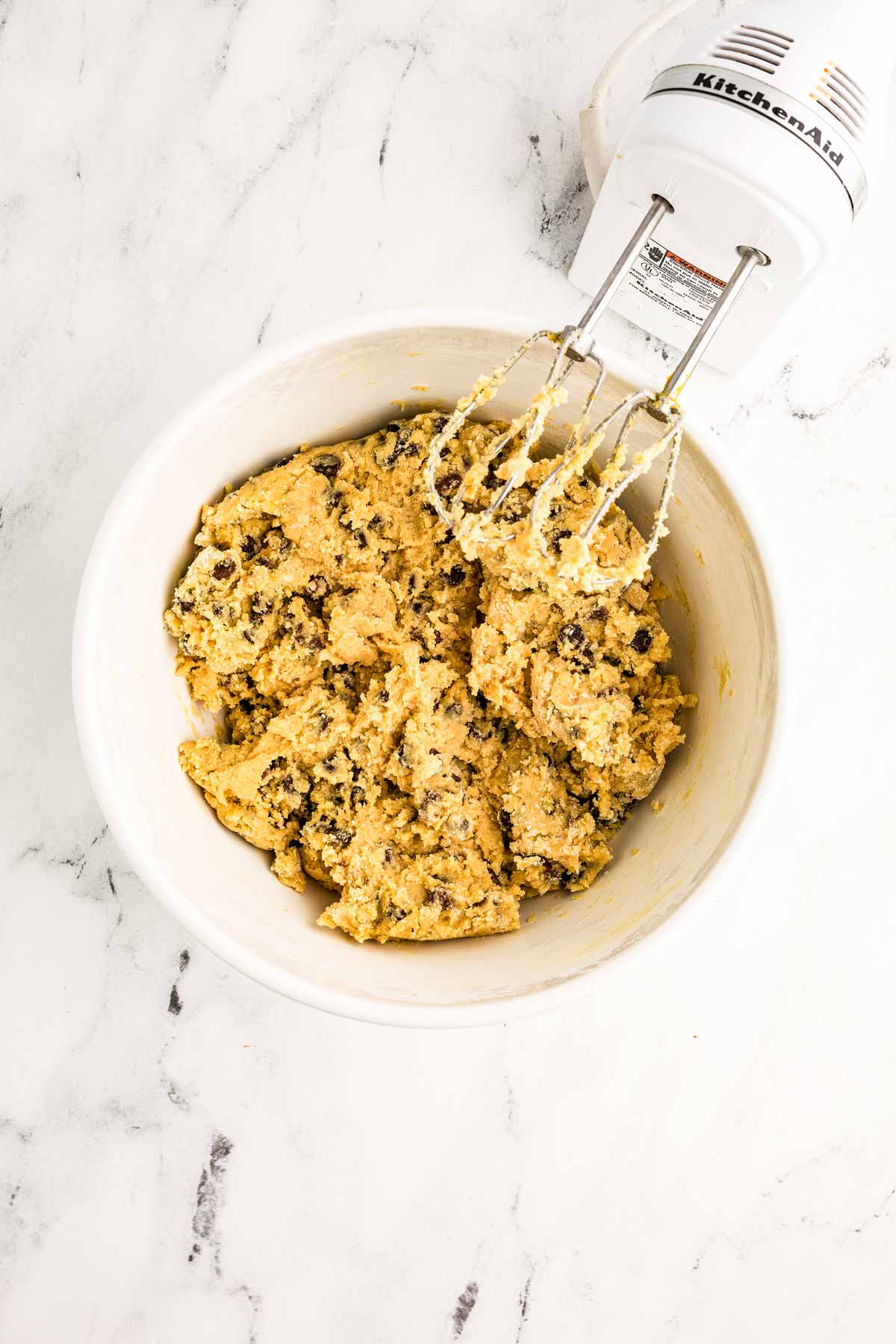 overhead view of chocolate chip cookie dough in white bowl with electric mixer next to it