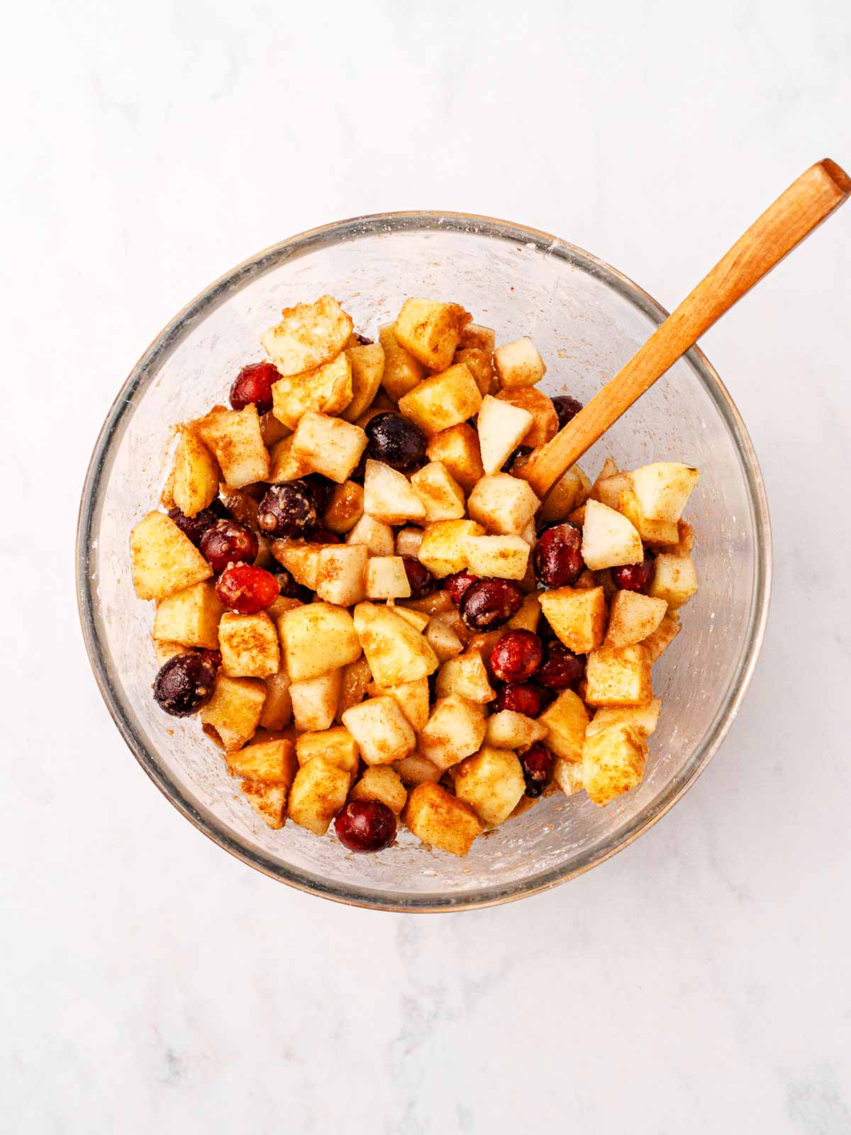 overhead view of apple cranberry crisp fruit filling in glass bowl with wooden spoon