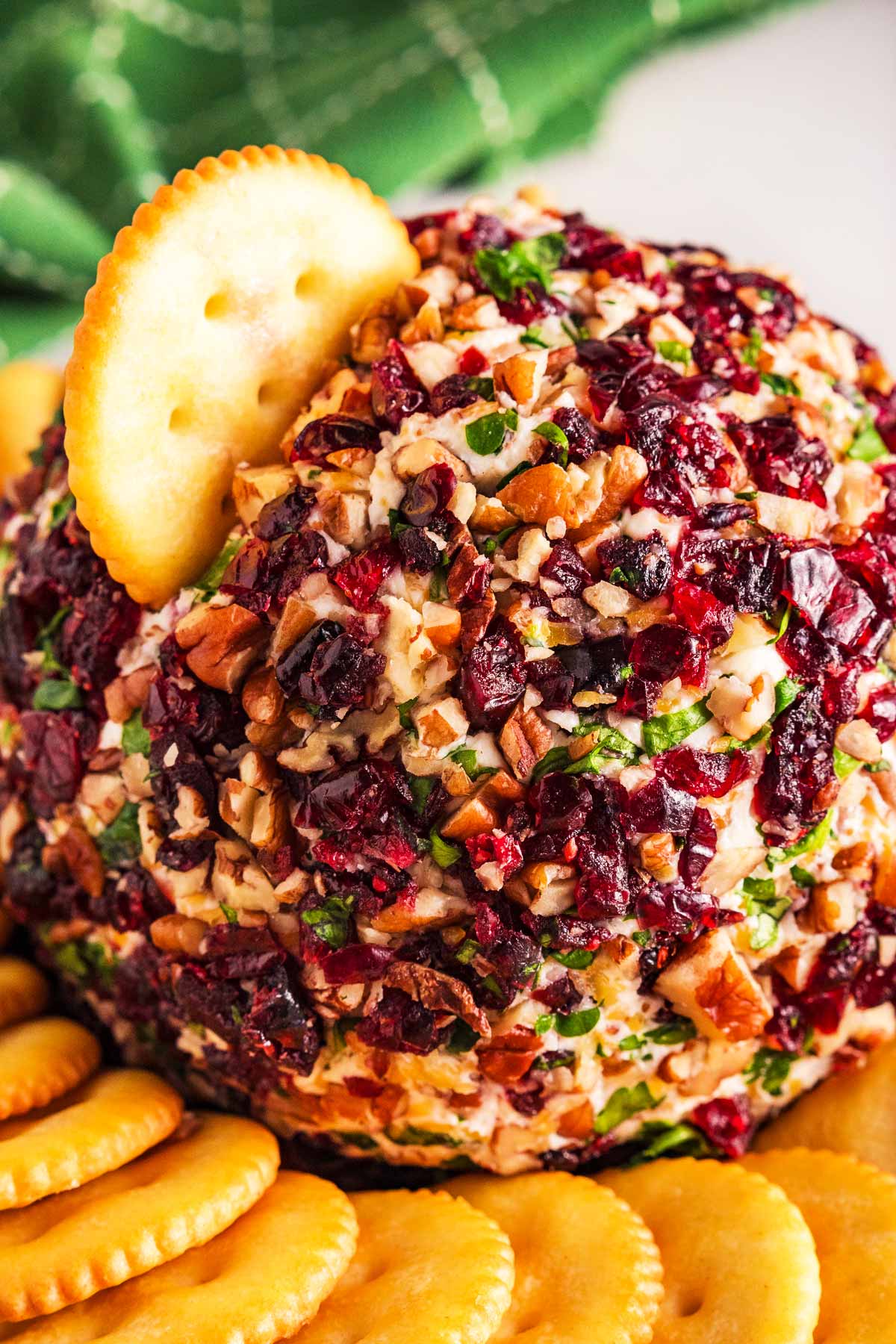 frontal close up view of cranberry pecan cheeseball with cracker stuck in