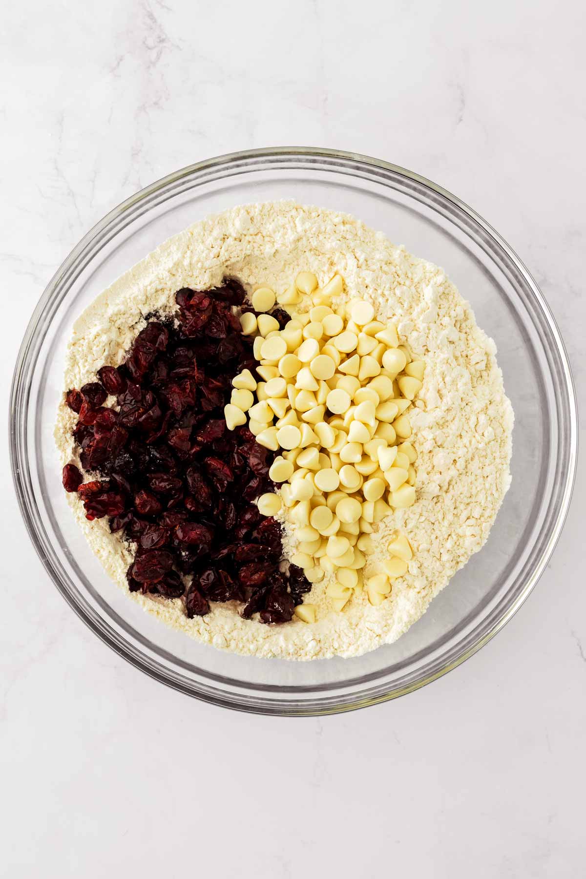 overhead view of dry cookie ingredients with dried cranberries and white chocolate chips in glass bowl