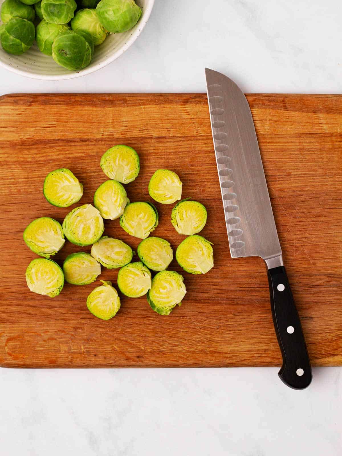 overhead view of sliced Brussels sprouts on wooden chopping board with knife