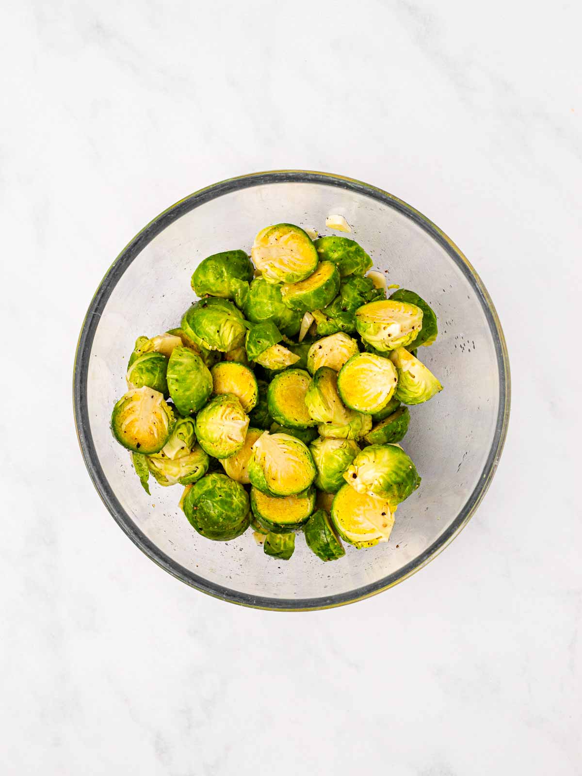 overhead view of seasoned raw Brussels sprouts in glass bowl