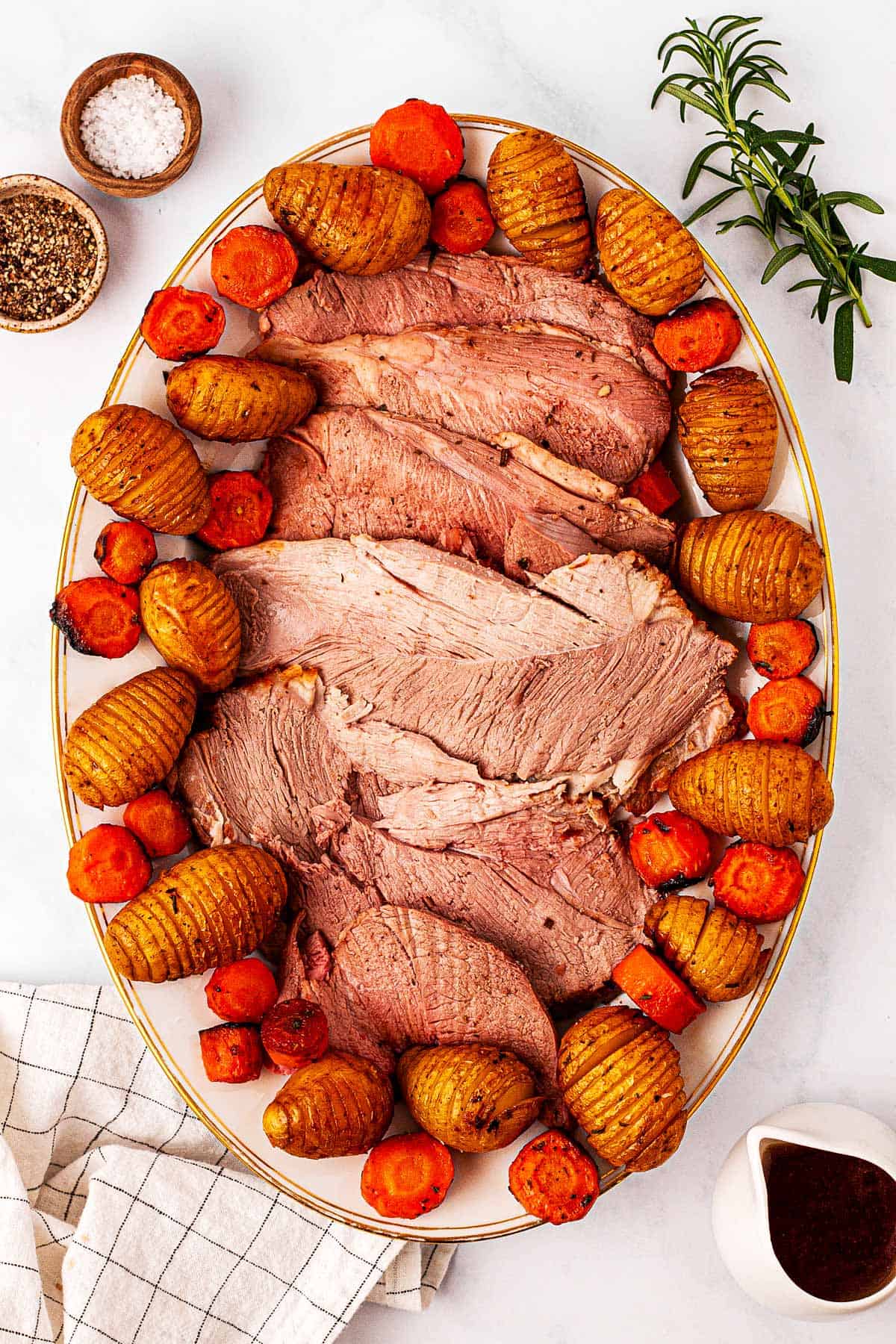 overhead view of sliced leg of lamb on platter with potatoes and carrots