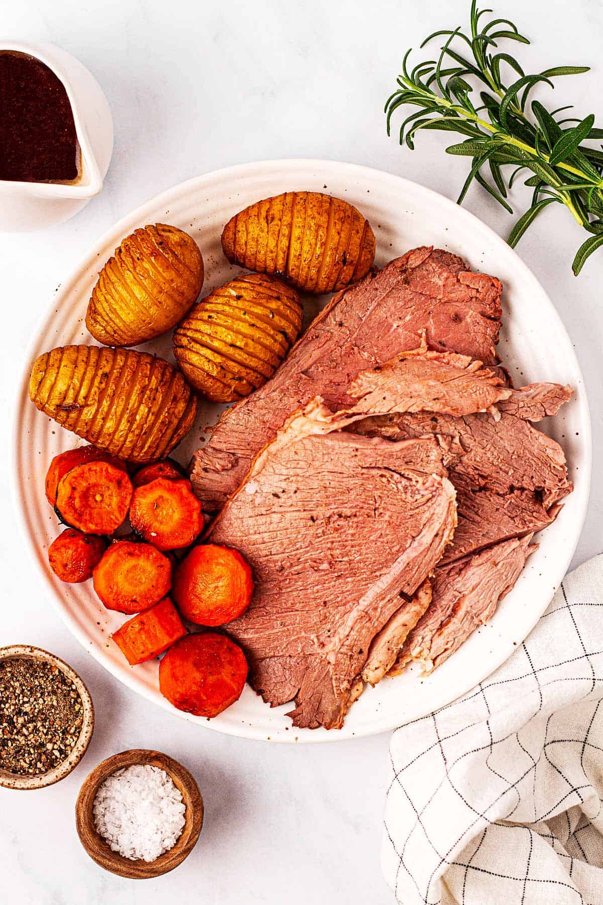 overhead view of roasted leg of lamb slices with potatoes and carrots on white plate