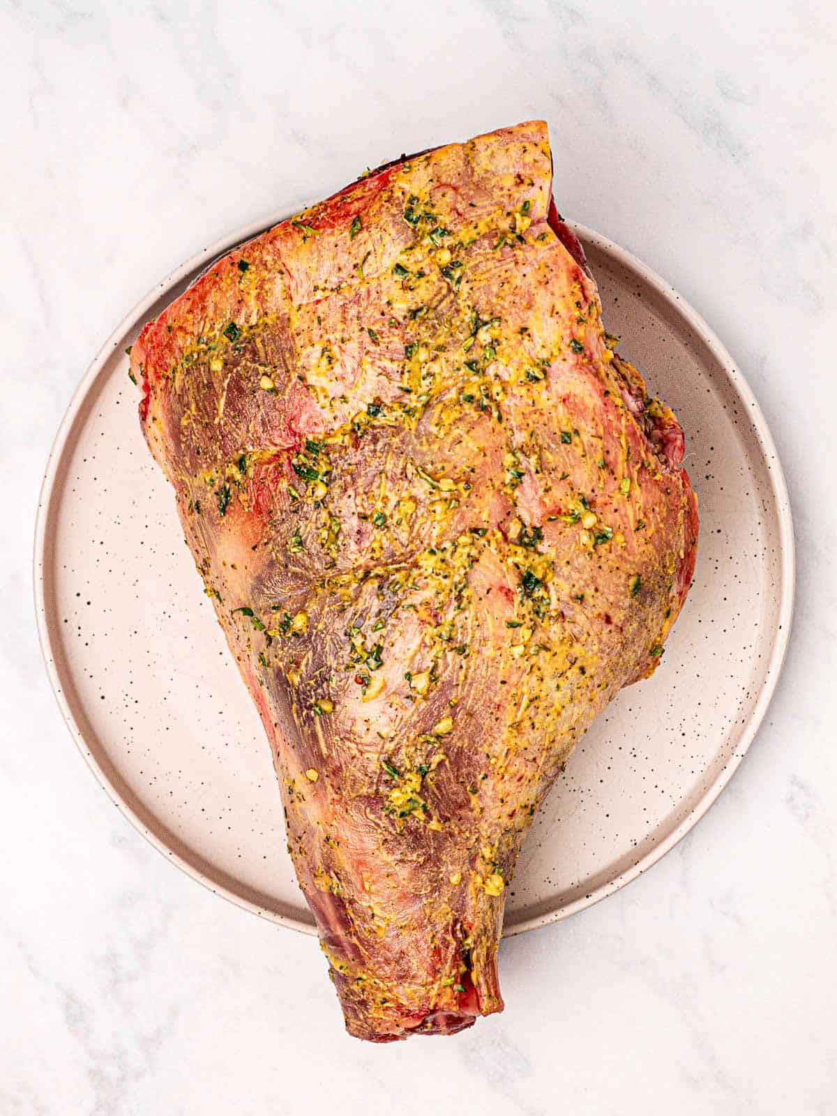 overhead view of raw leg of lamb covered in seasoning