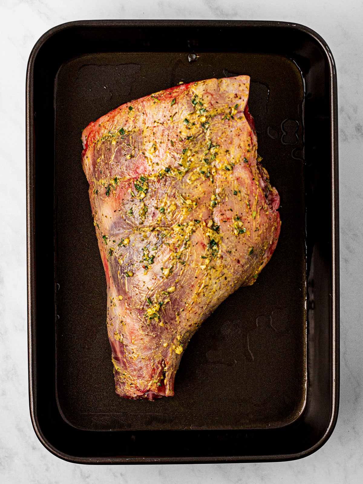 overhead view of raw leg of lamb on black roasting pan