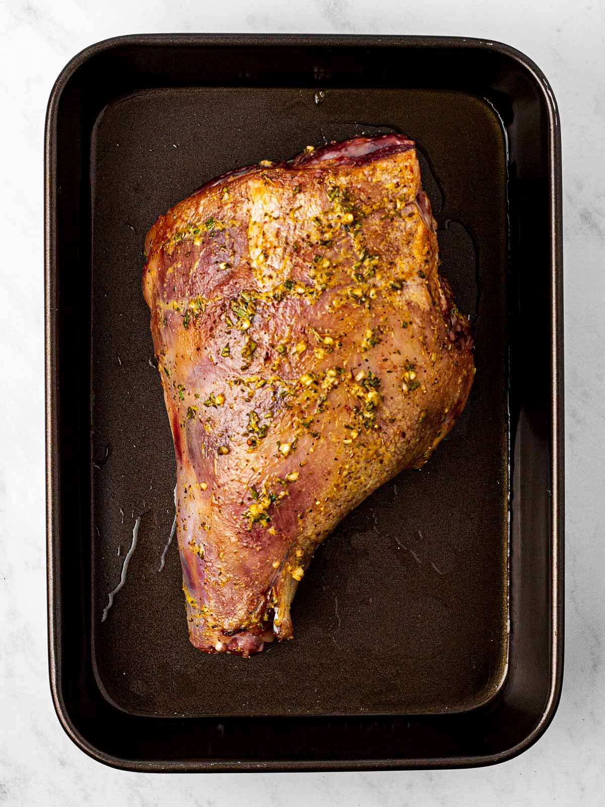 overhead view of seared leg of lamb on black roasting pan