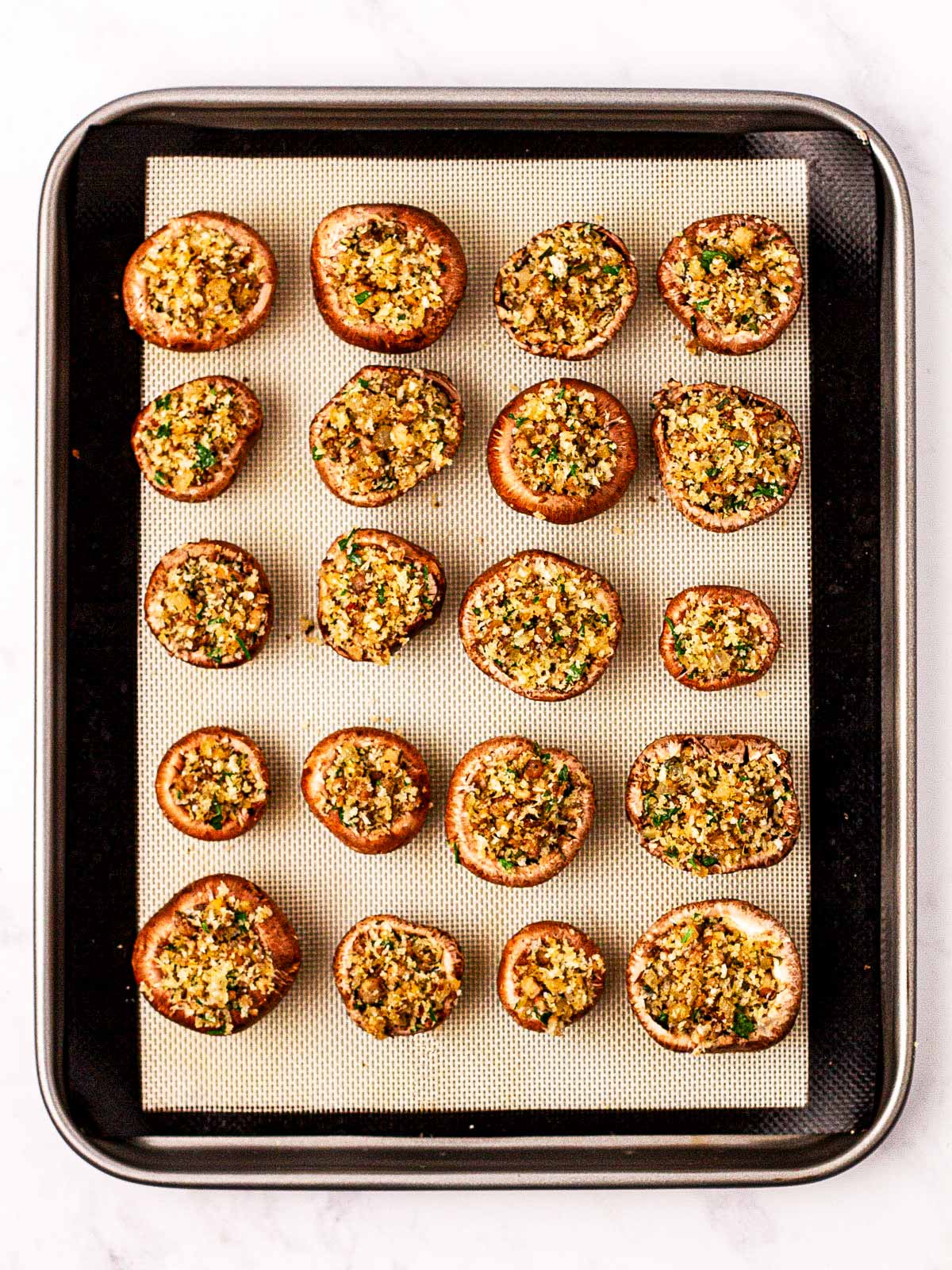 overhead view of unbaked stuffed mushrooms on lined baking sheet