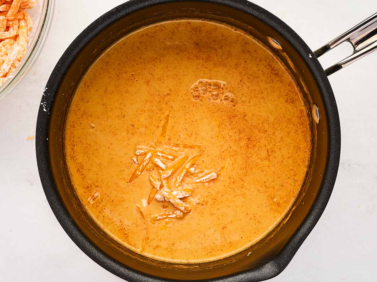 overhead view of shredded cheese being added to saucepan in small handfuls