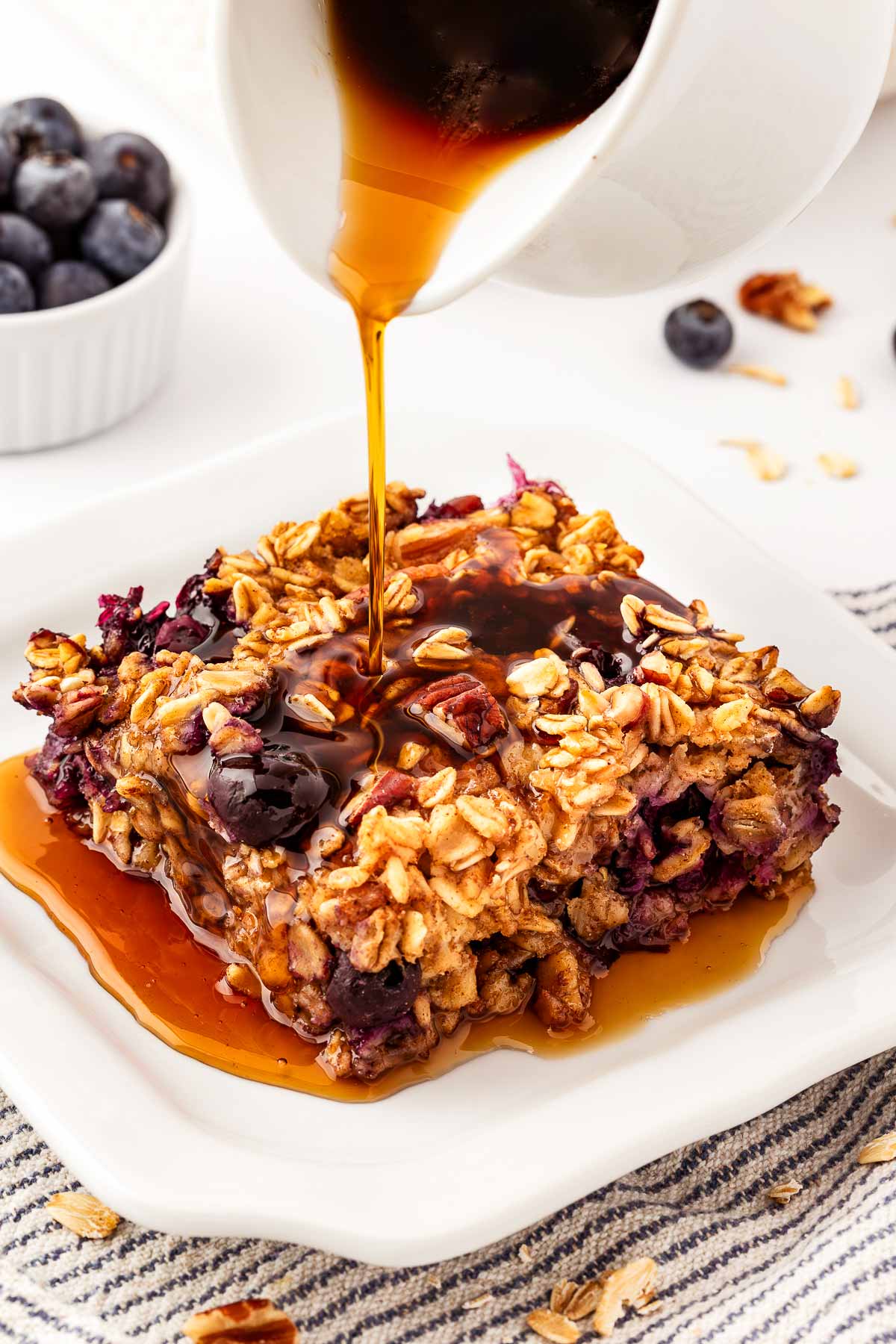 frontal view of maple syrup pouring over slice of blueberry baked oatmeal