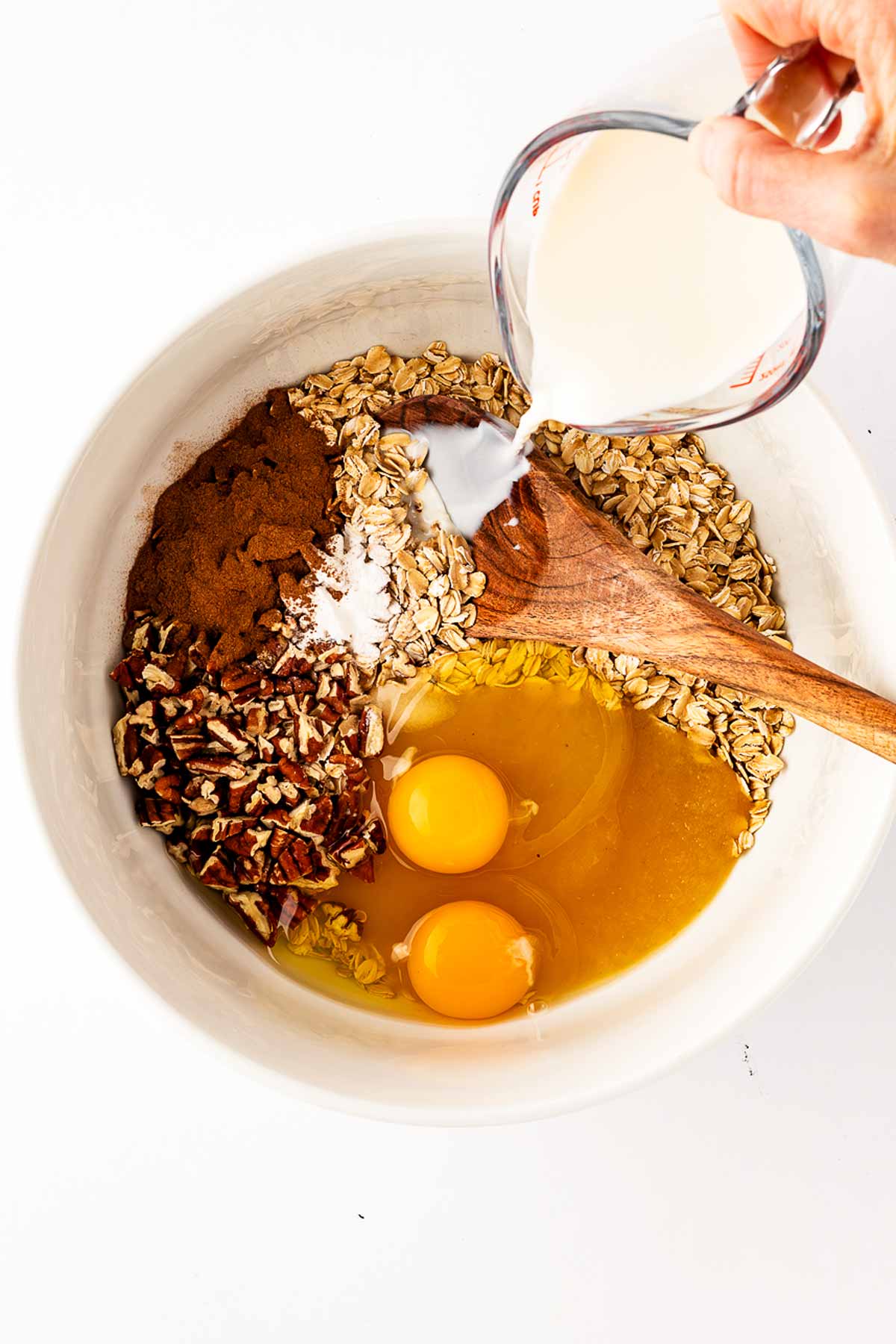 overhead view of female hand pouring milk into bowl with oats and eggs