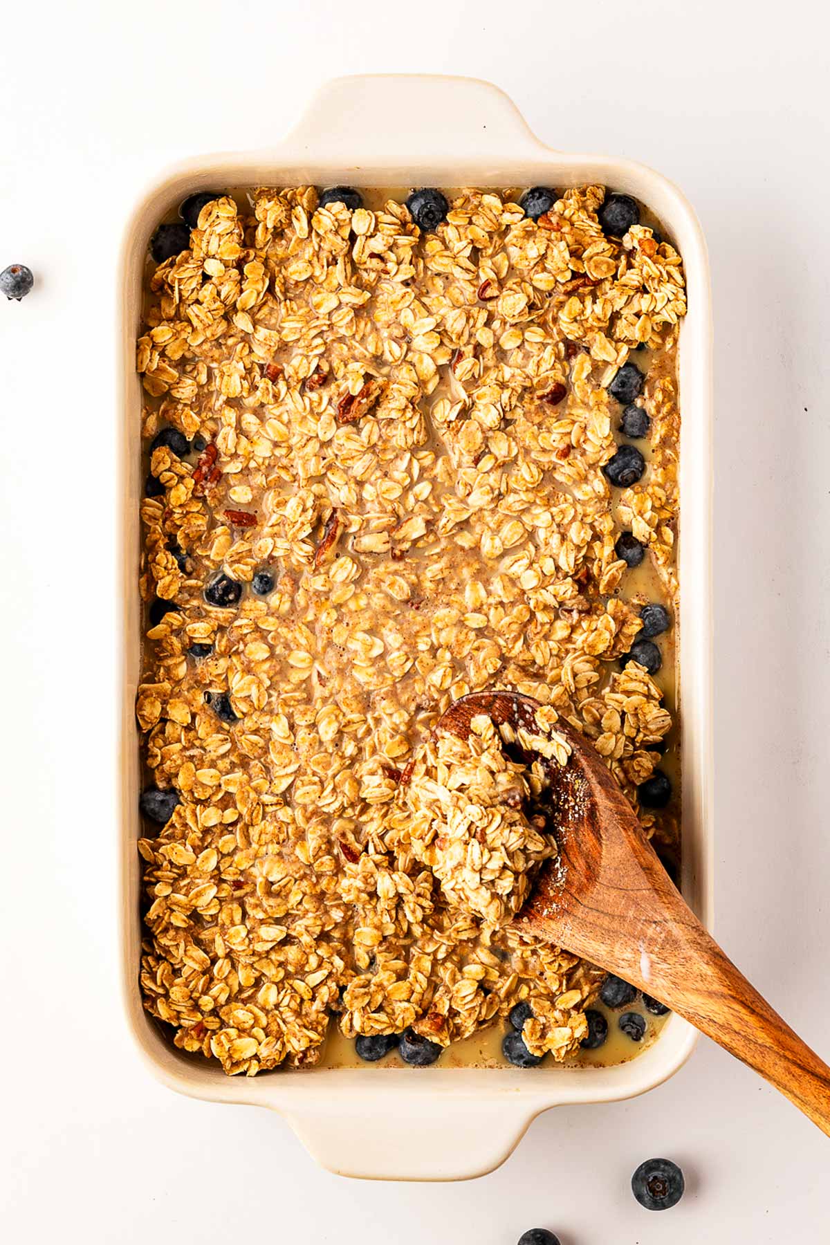 overhead view of wooden spoon spooning oatmeal mixture into baking dish