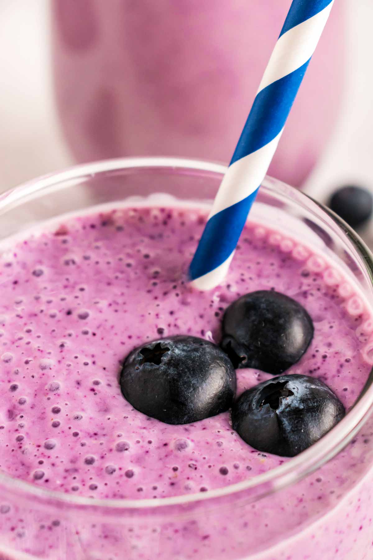 frontal close up shot of blueberry smoothie in glass with straw