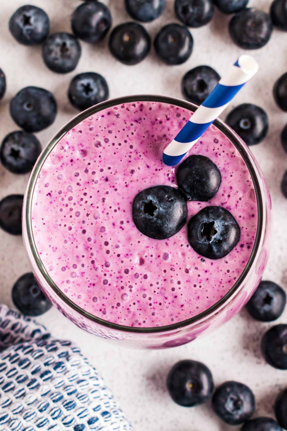 overhead view of blueberry smoothie in glass surrounded by blueberries