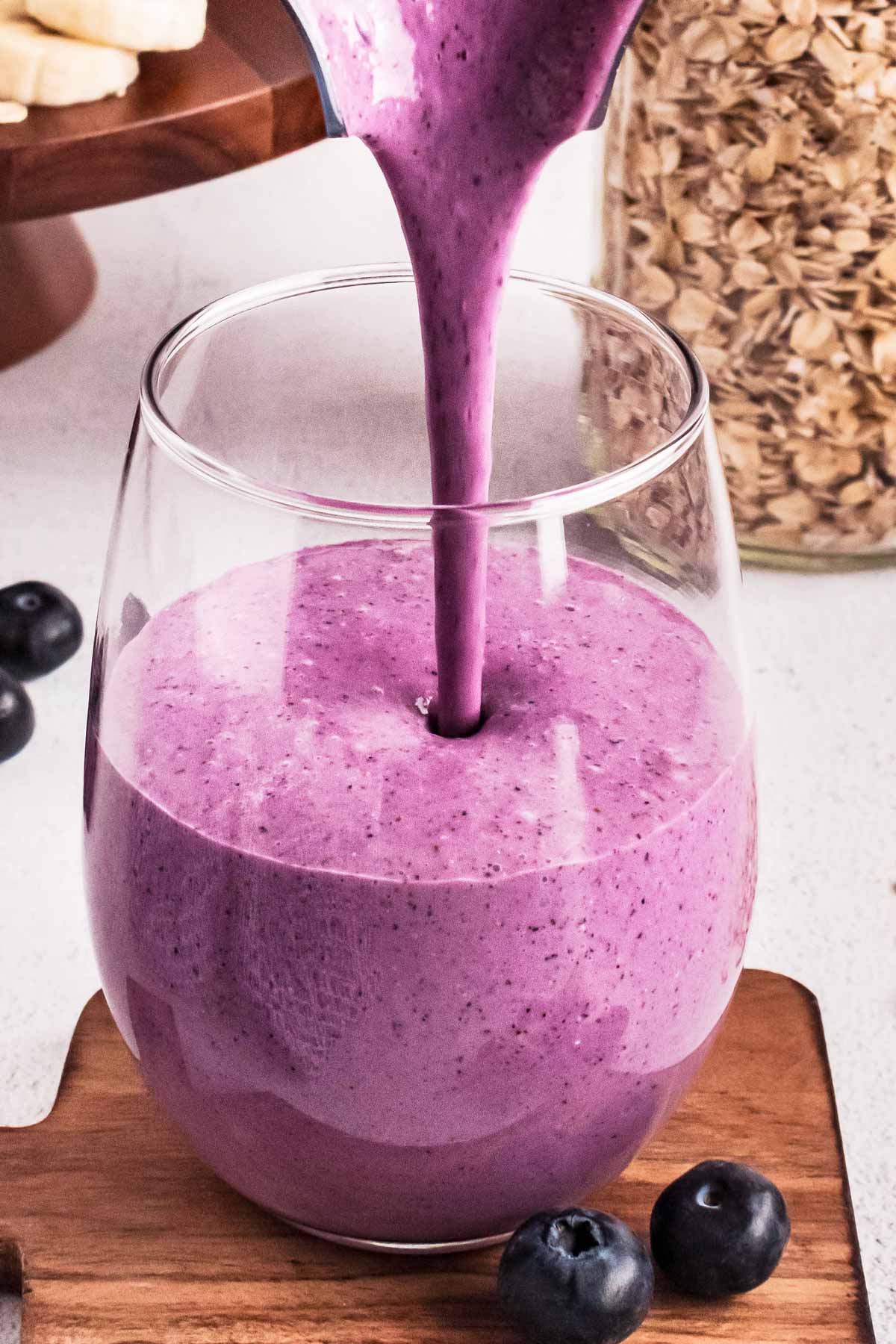 frontal view of blueberry smoothie pouring from blender into glass