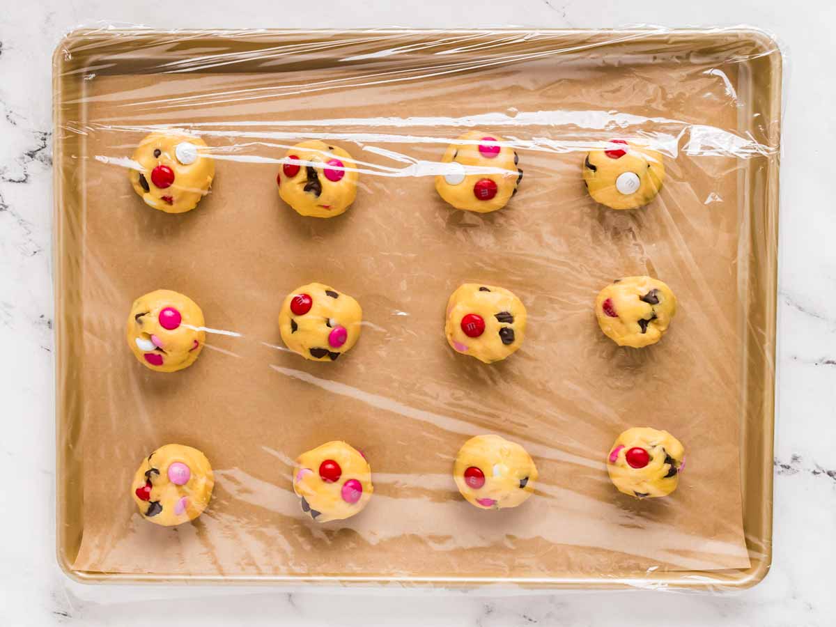 overhead view of plastic wrap covered cookie dough balls on lined baking sheet