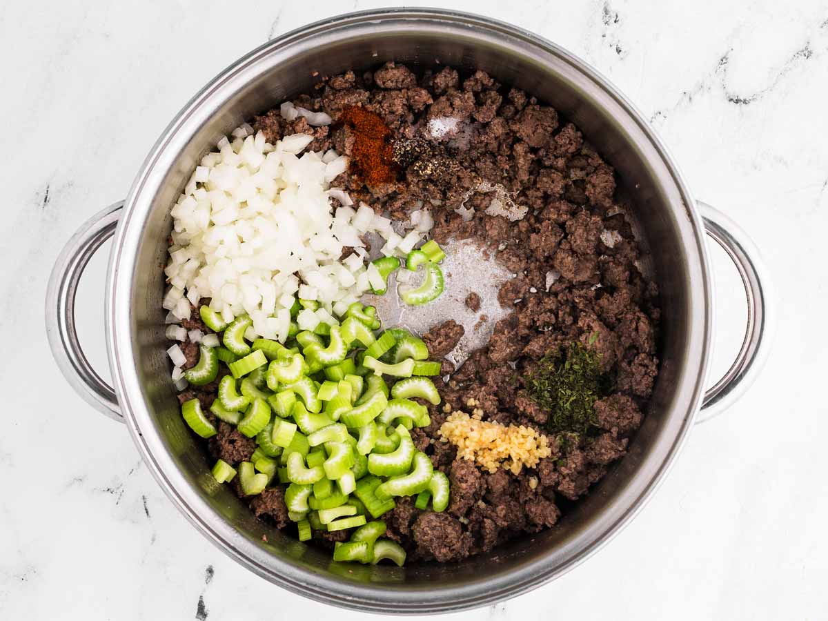 overhead view of browned ground beef in soup pot with diced onion and celery