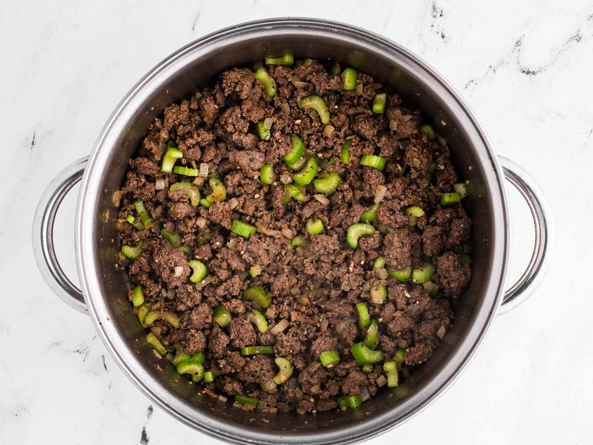 overhead view of browned ground beef in soup pot with cooked diced onion and celery