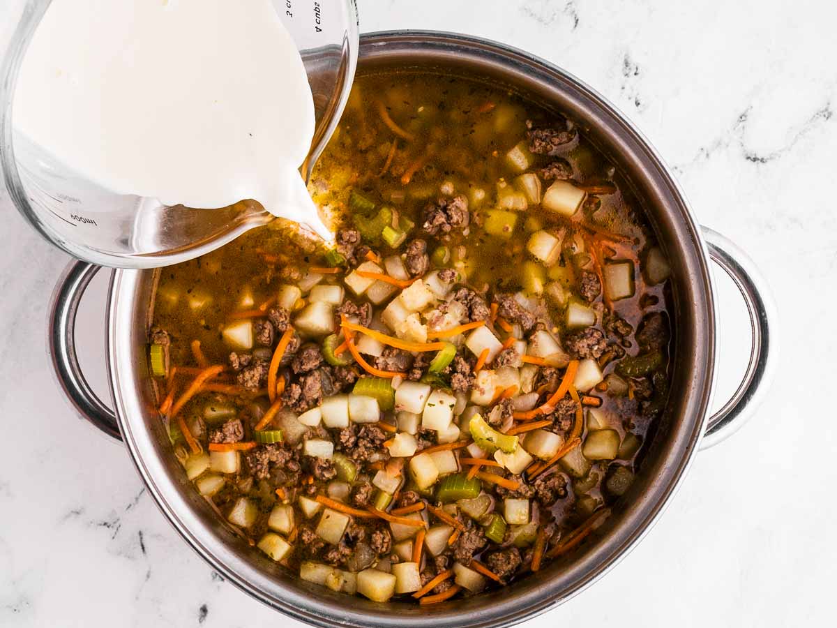 overhead view of cornstarch slurry pouring into pot with soup