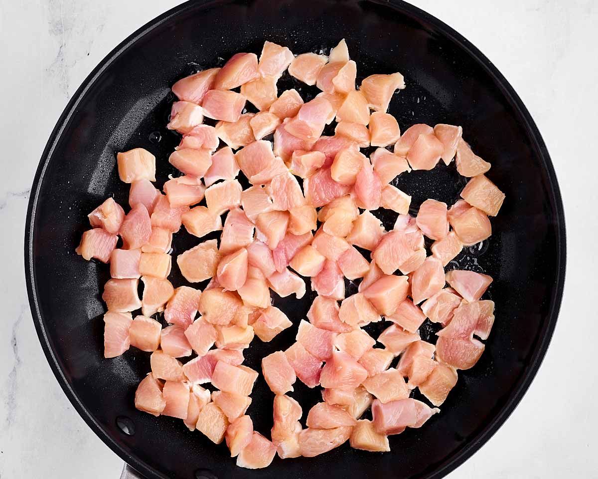 overhead view of uncooked diced chicken in skillet