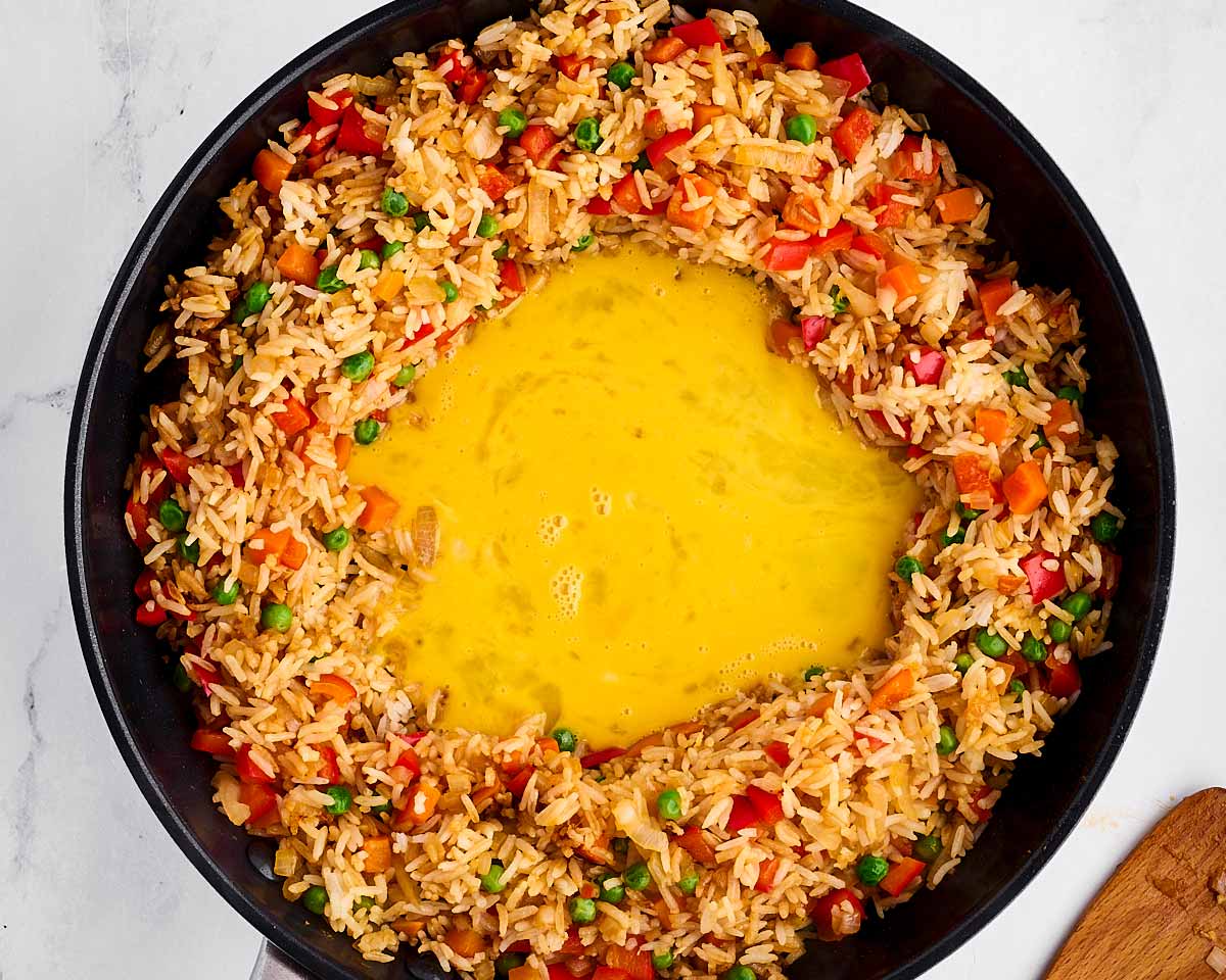 overhead view of uncooked scrambled eggs in middle of rice and vegetables in skillet