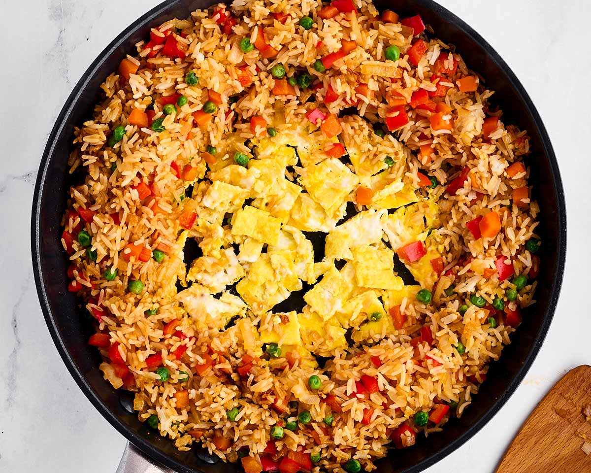 overhead view of cooked scrambled eggs in middle of rice and vegetables in skillet