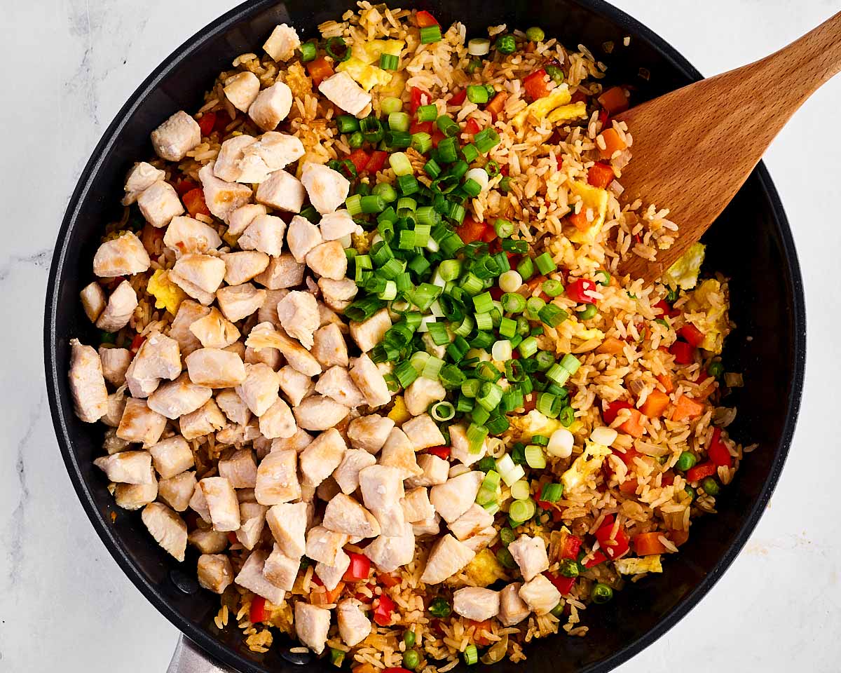 overhead view of chicken and green onion on top of fried rice in skillet