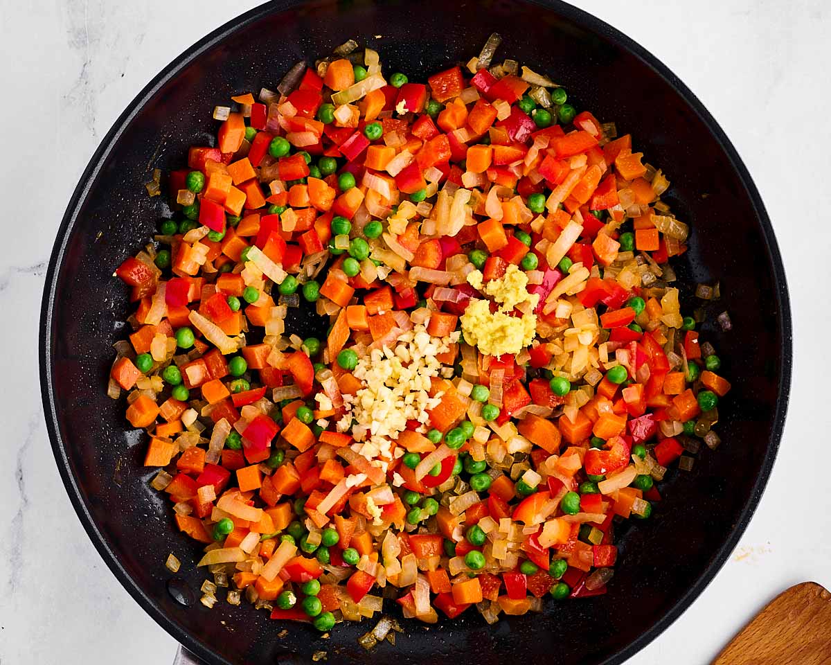 overhead view of minced garlic and ginger on top of cooked vegetables in skillet