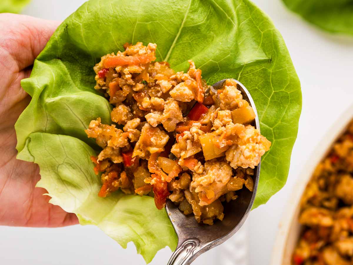 overhead view of female hand spooning chicken filling onto butter lettuce leaf