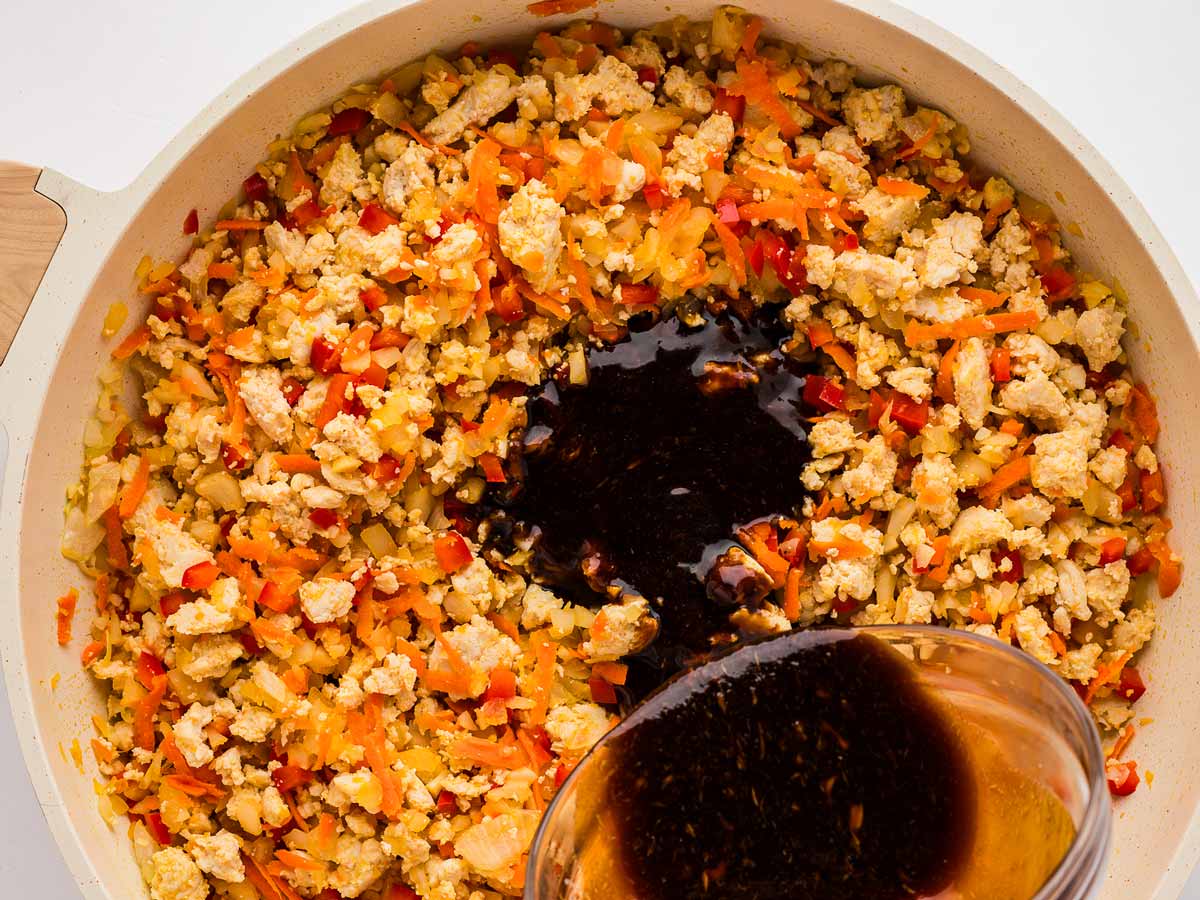 stir fry sauce being poured into skillet with ground chicken and vegetables