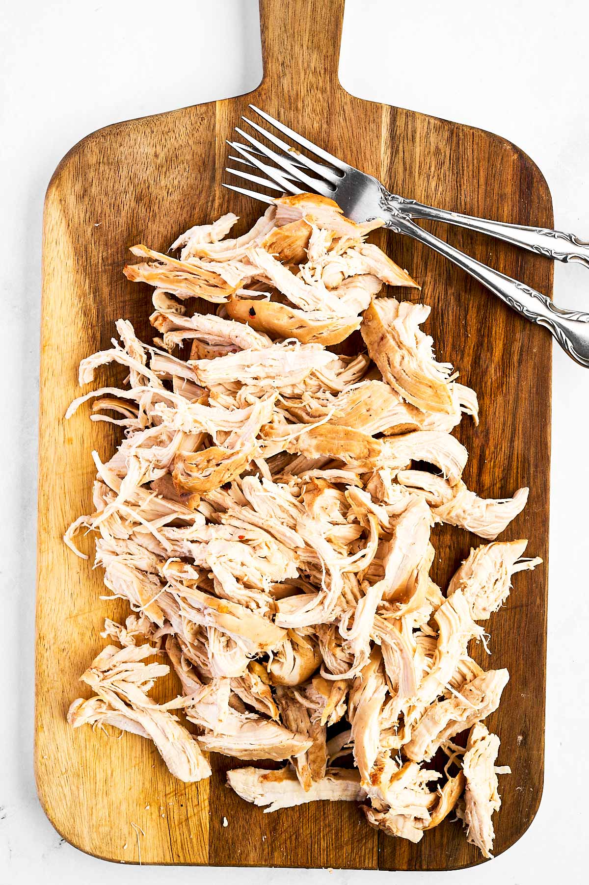 overhead view of shredded chicken on wooden cutting board