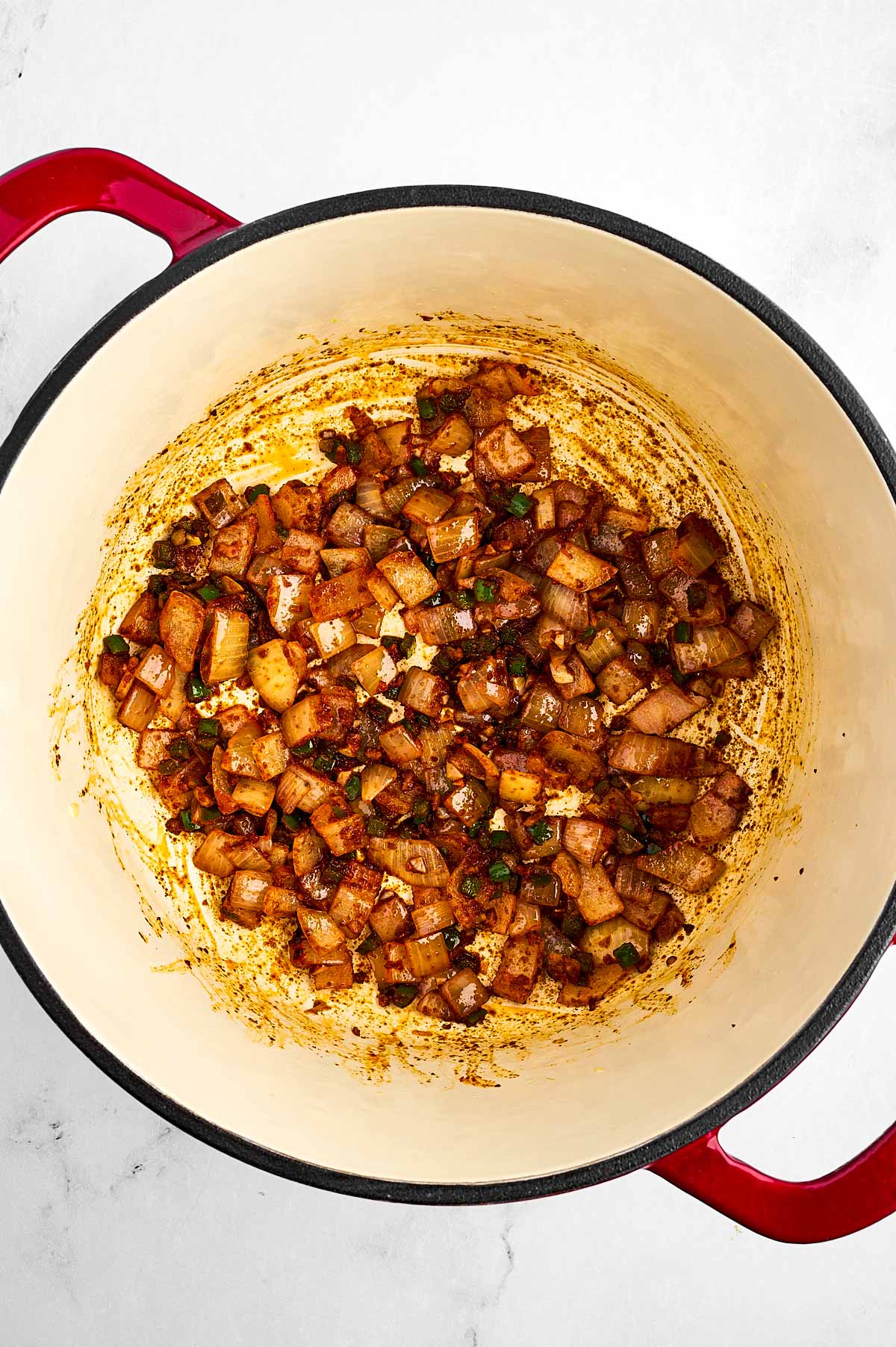 overhead view of cooked aromatics in pot stirred together with spices