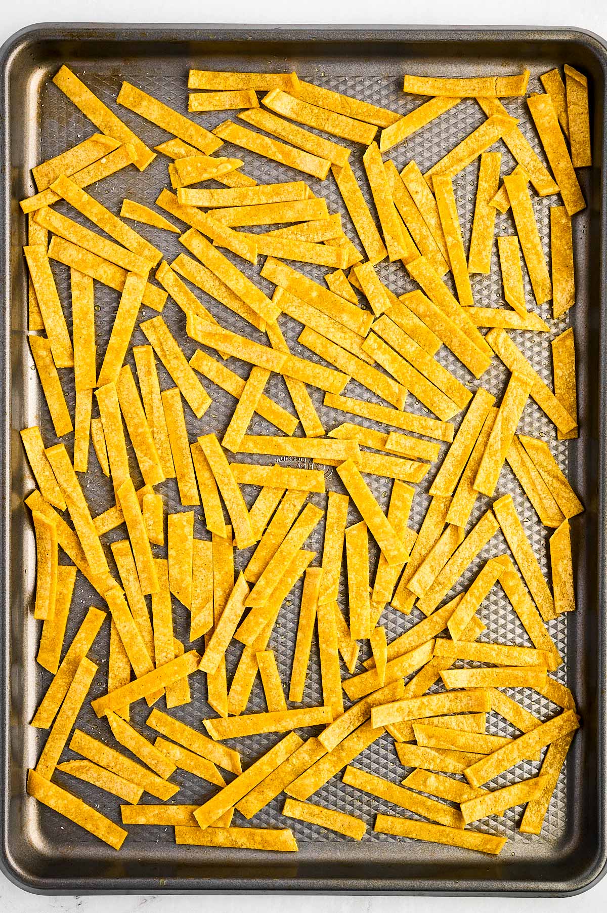 overhead view of unbaked tortilla strips on baking sheet