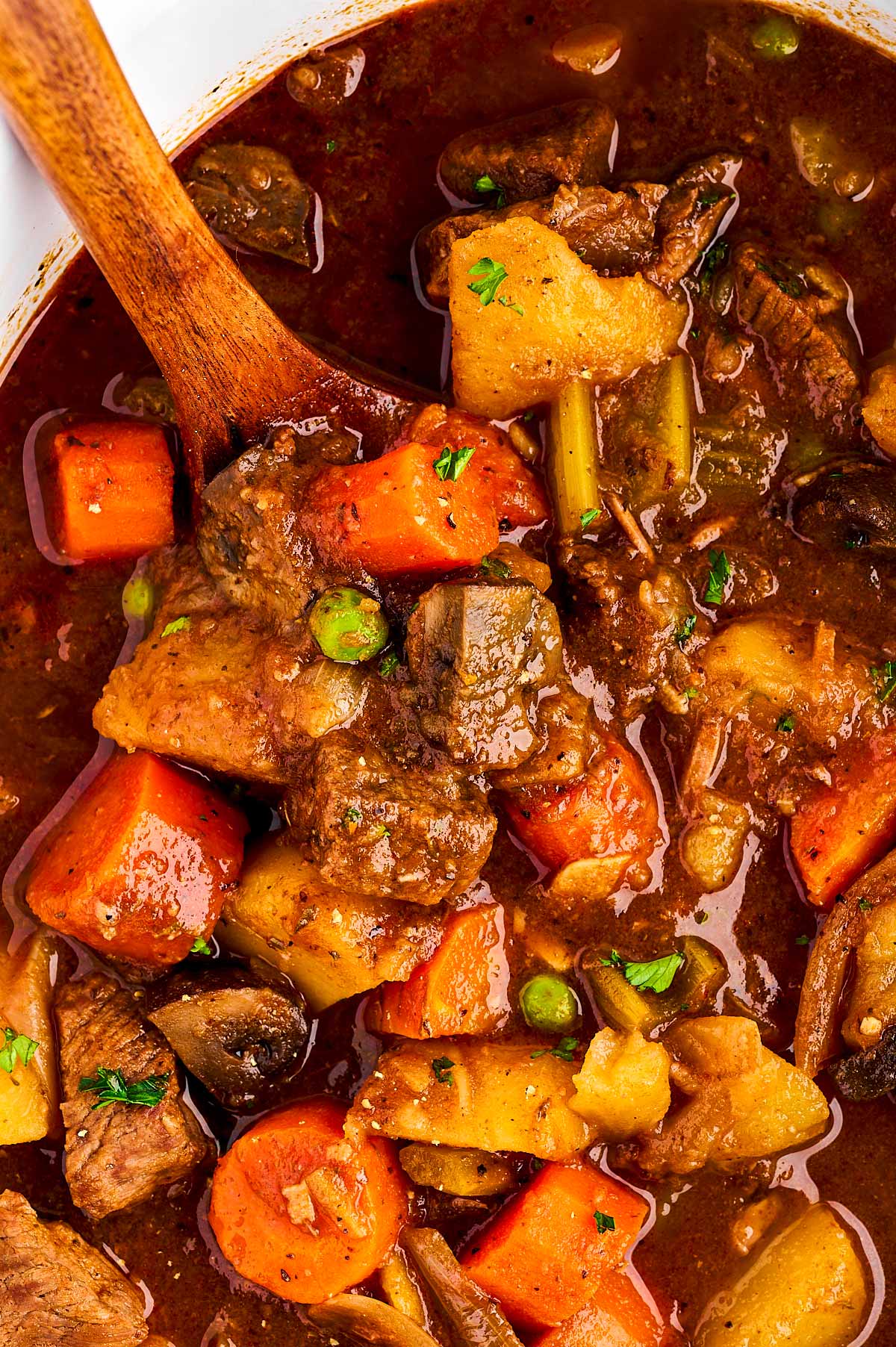 overhead view of beef stew being served from slow cooker with wooden spoon