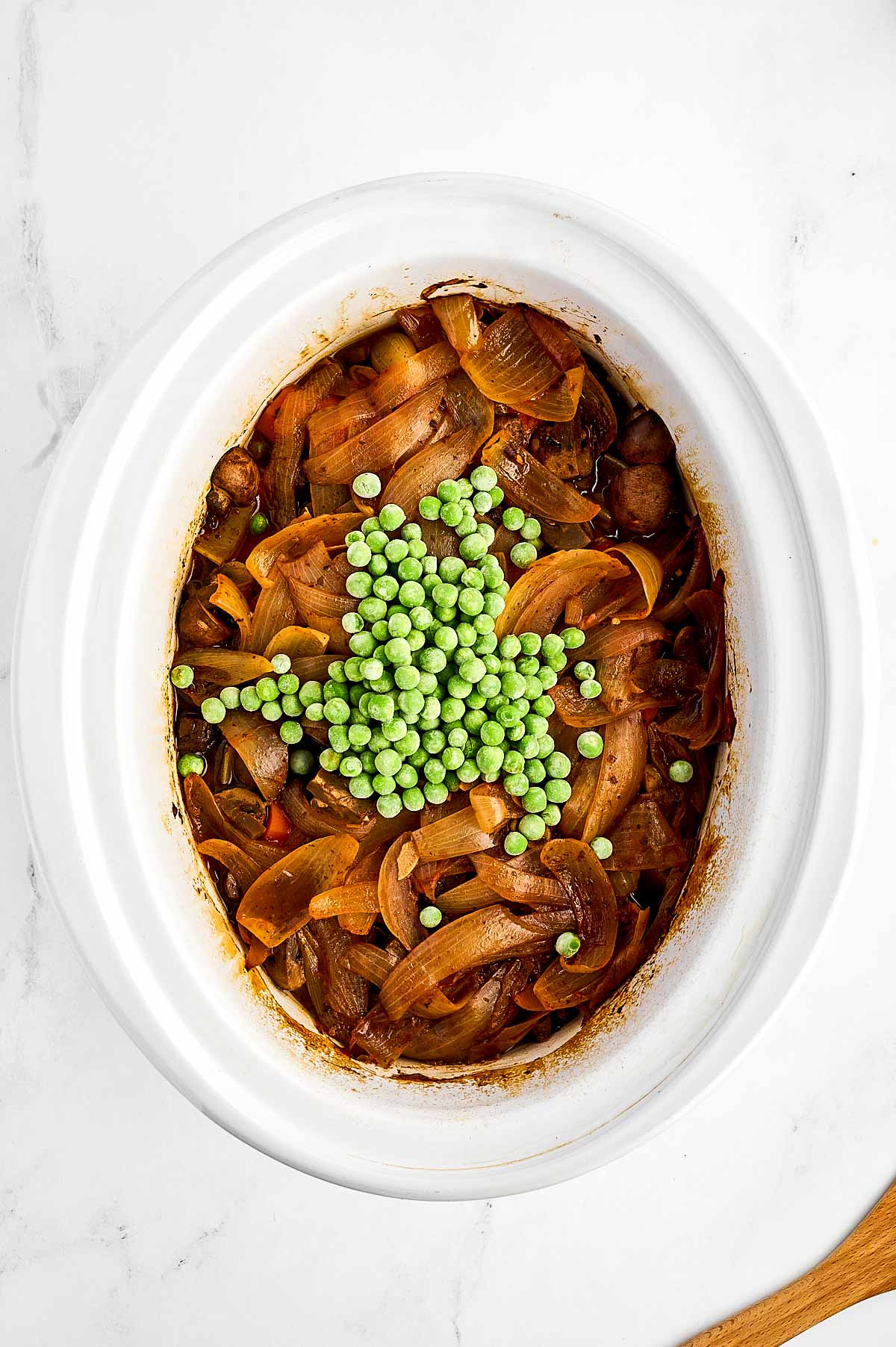 overhead view of frozen peas on top of beef stew in slow cooker