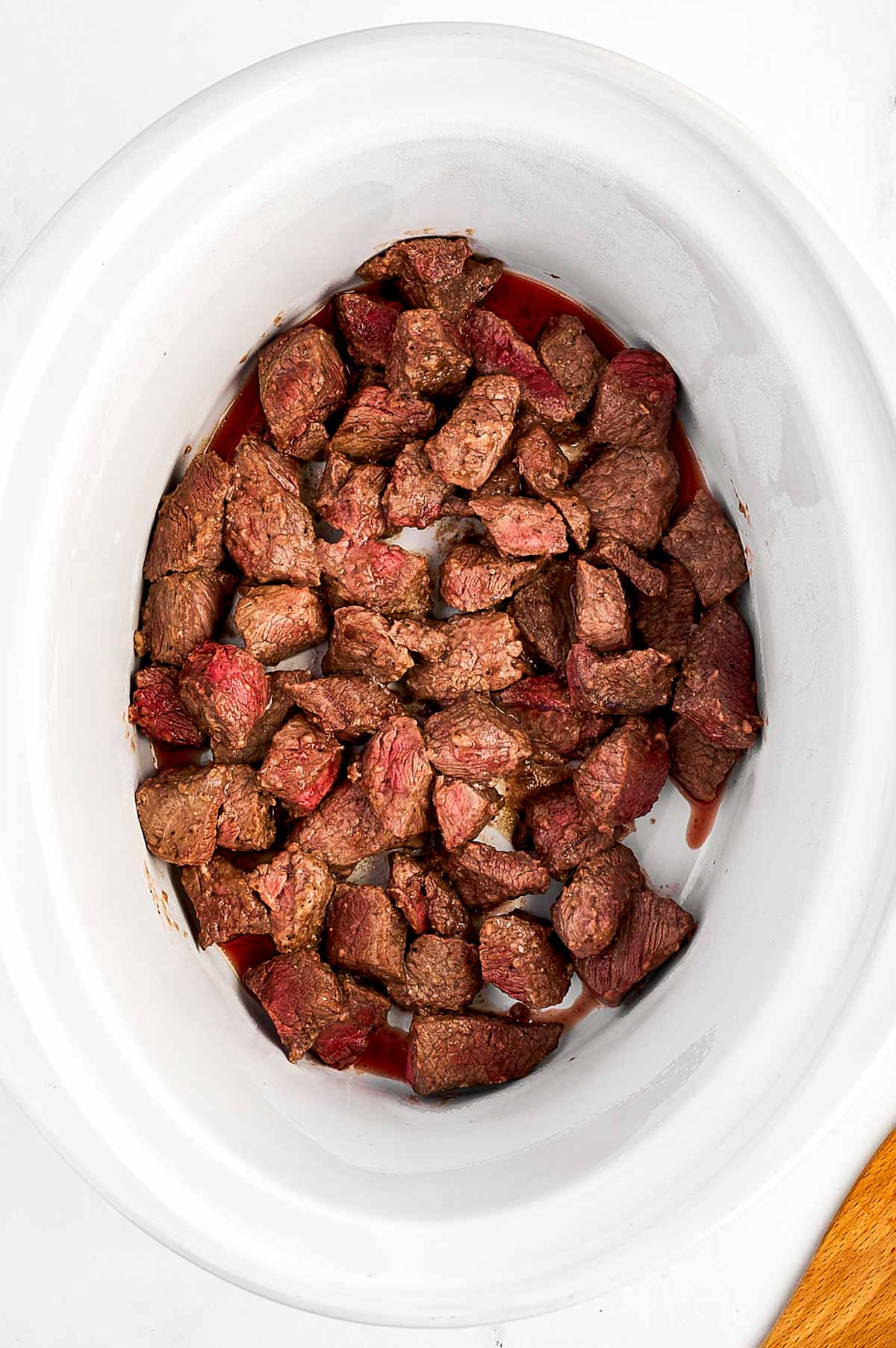 overhead view of browned beef cubes in slow cooker