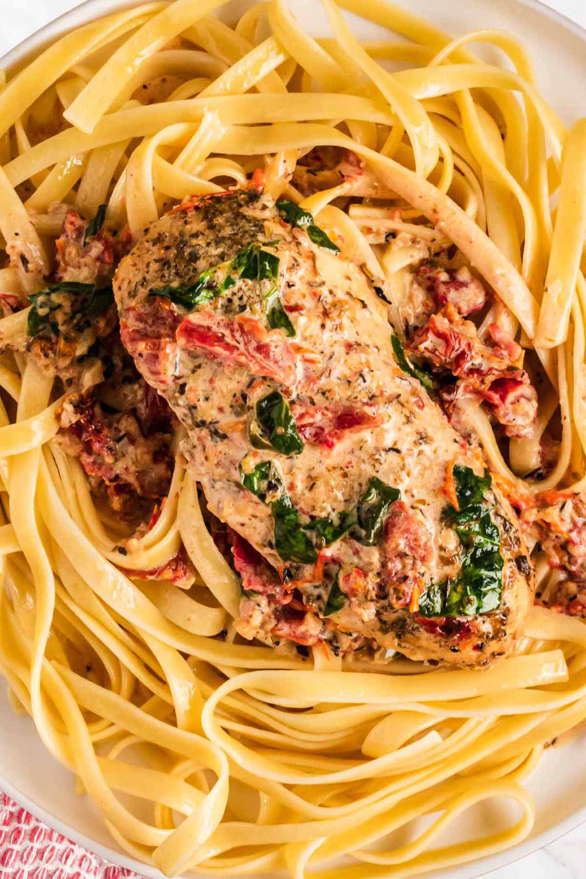 overhead view of chicken breast on top of pasta with tuscan cream sauce