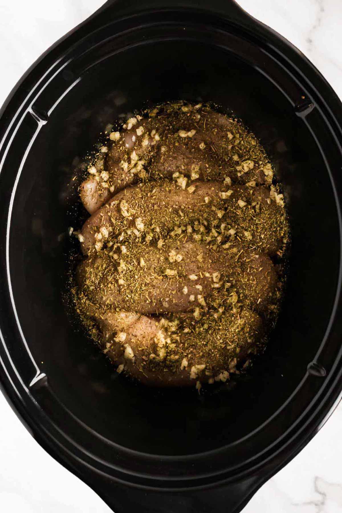 overhead view of seasoned chicken breasts in slow cooker