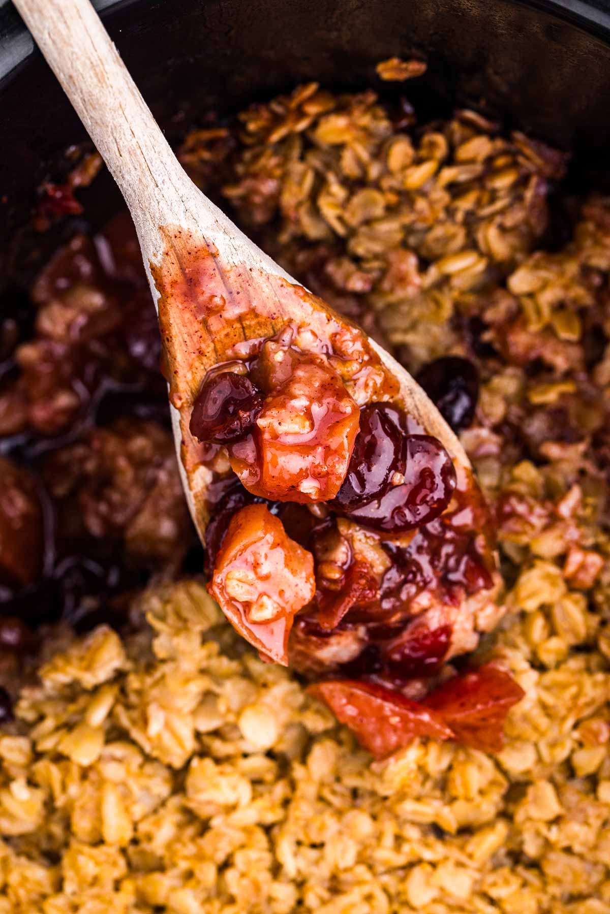 overhead view of wooden spoon scooping apple oatmeal from black crockery dish