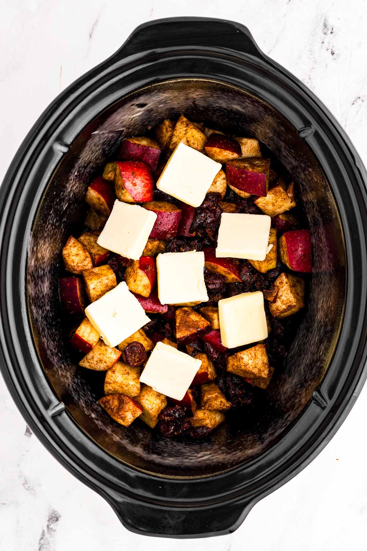 overhead view of apples in slow cooker crockery insert topped with butter