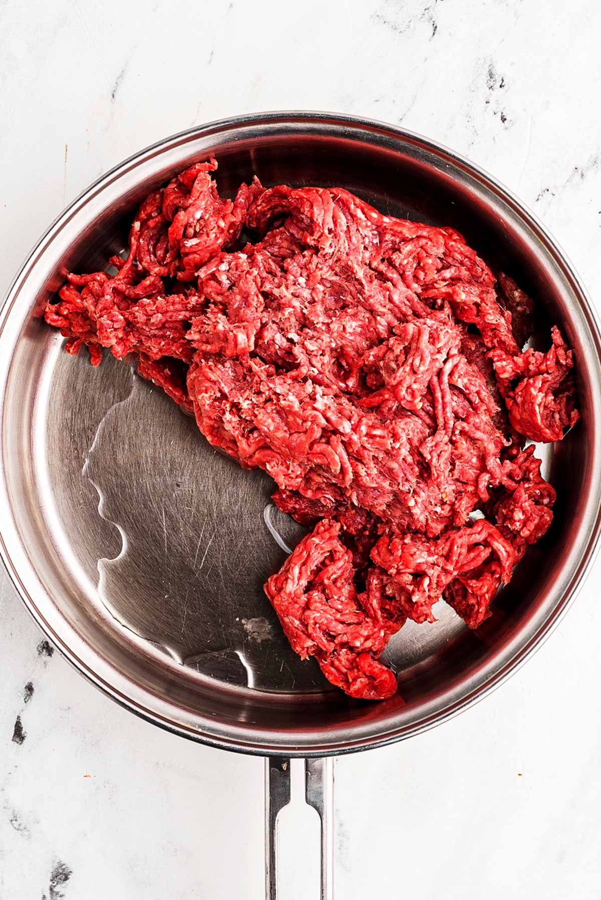 overhead view of raw ground beef in skillet with oil