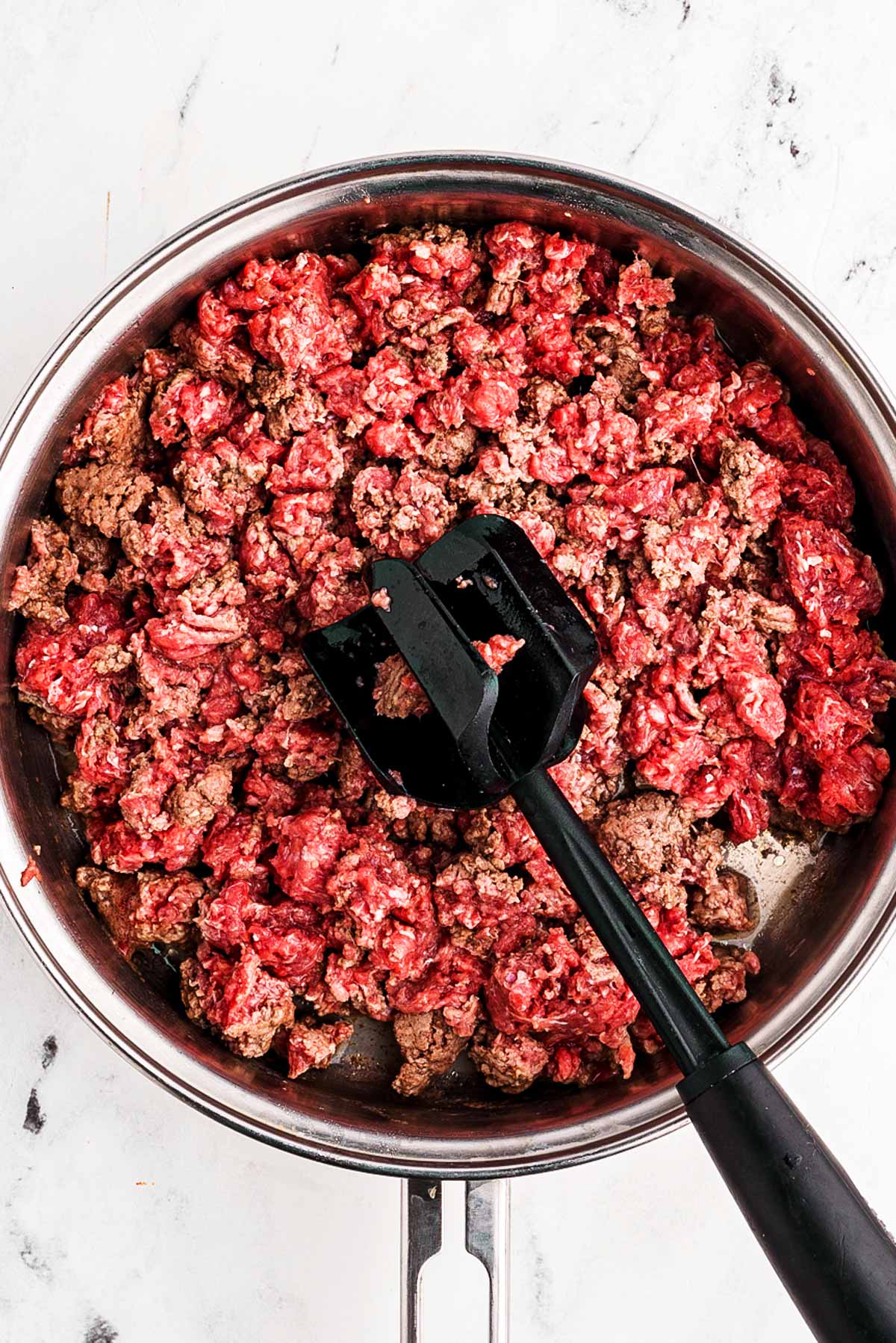 overhead view of browned ground beef in skillet with meat masher