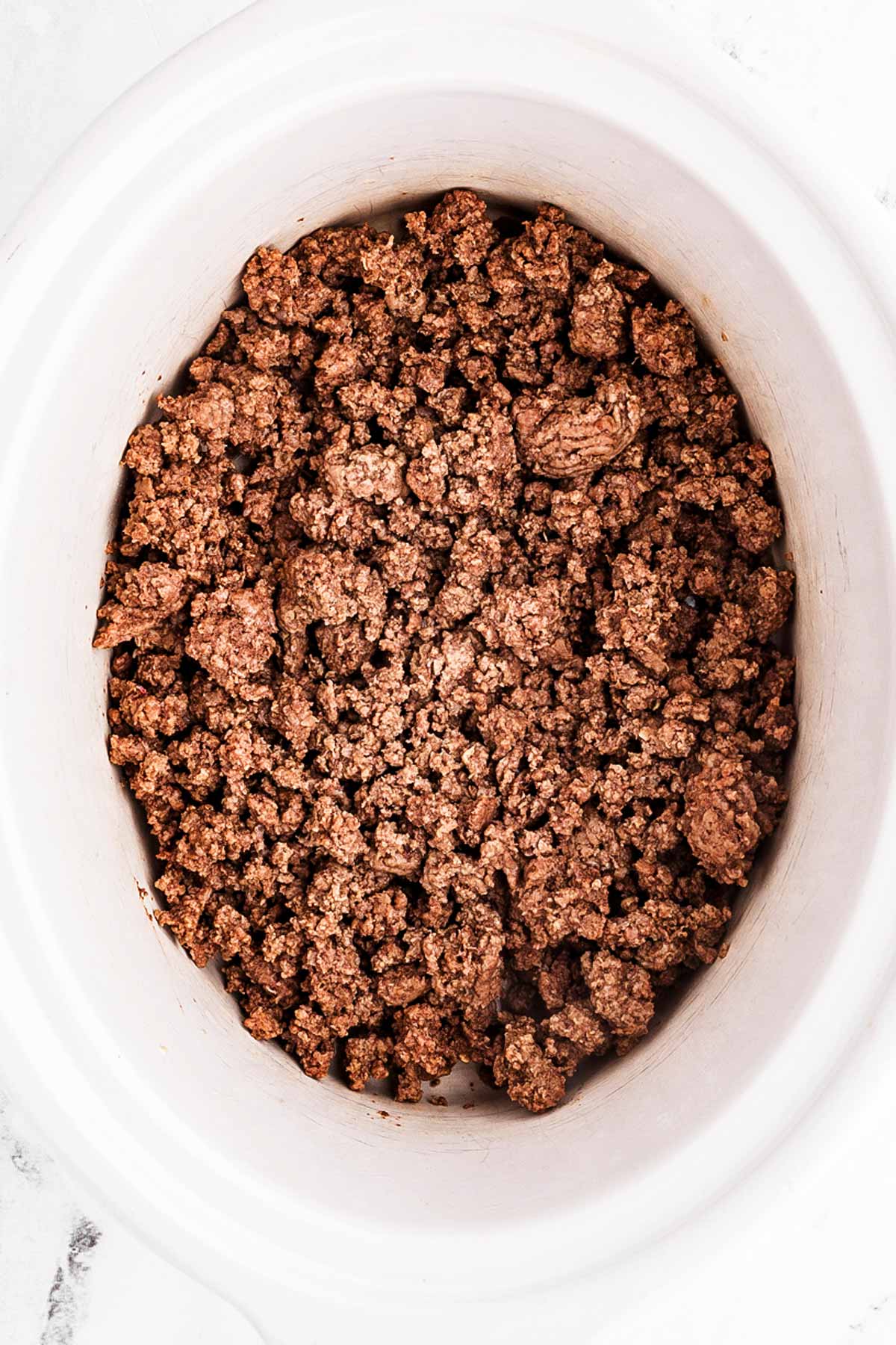 overhead view of browned ground beef being transferred to slow cooker