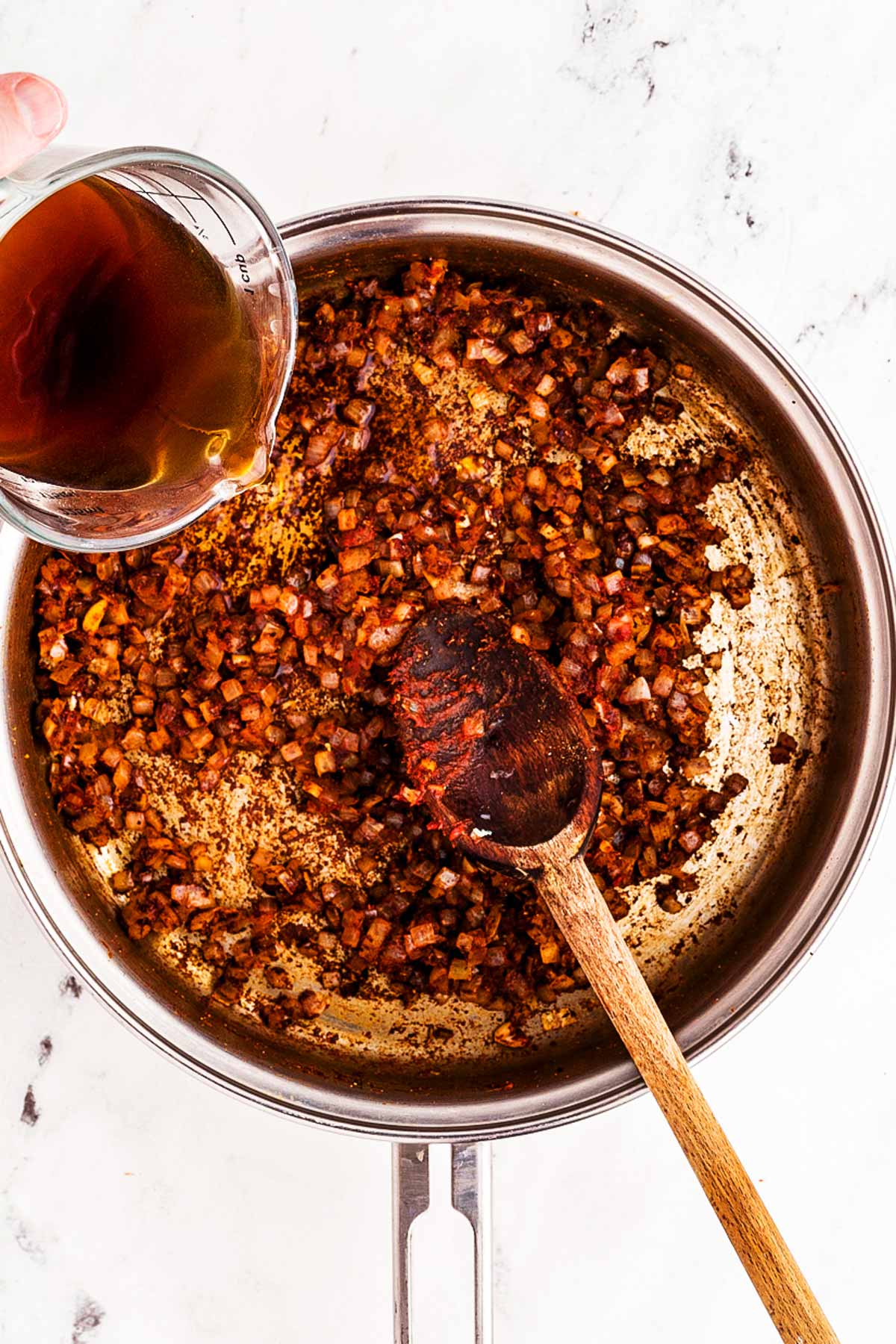 overhead view of beef broth being stirred into skillet with cooked onion and garlic