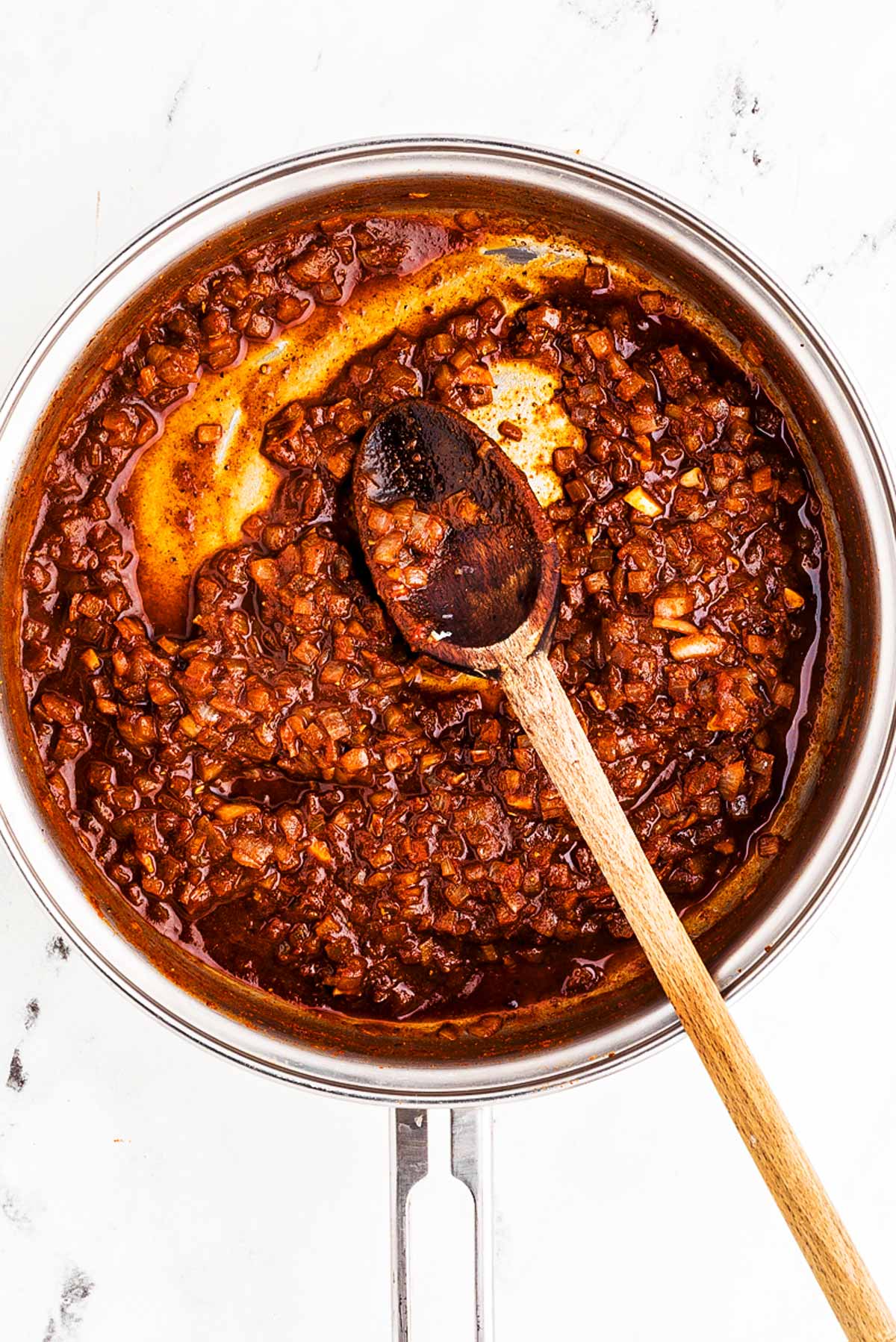 overhead view of cooked chili base in skillet with wooden spoon